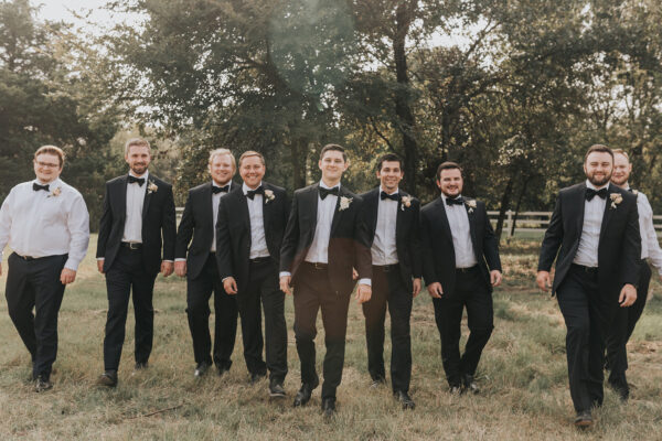groom and his side of the wedding party walk through the French farmhouse grounds
