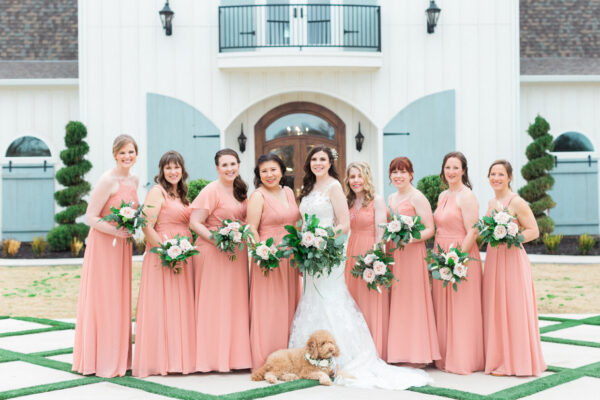 bride and bridesmaids pose in front of venue with brides dog