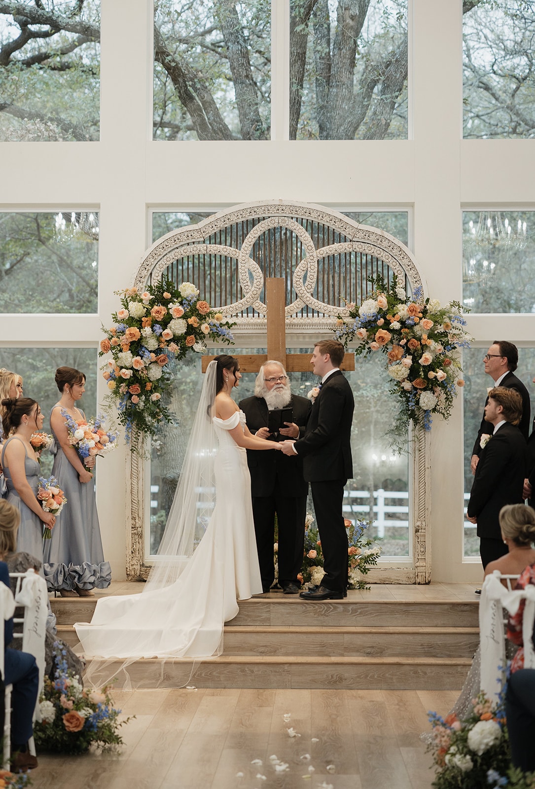 Avery and Pearson exchanging vows at the antique arch with lush peach and blue florals