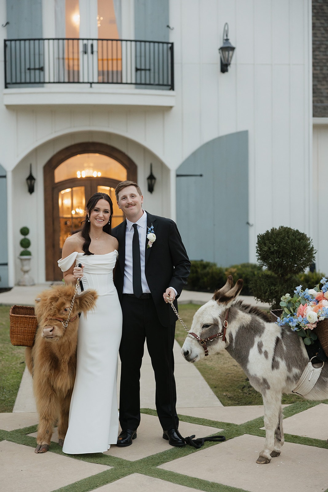 Avery and Pearson posing with a mini highland cow and a mini donkey in front of the venue