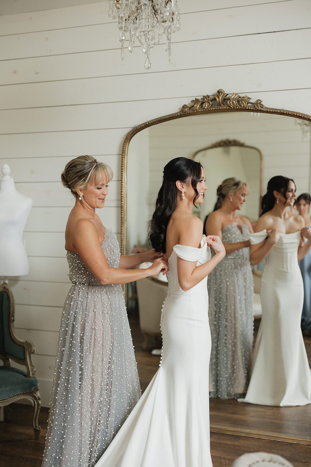 Avery getting her dress buttoned in the bridal suite with her mom and bridesmaids reflected in the gold mirror