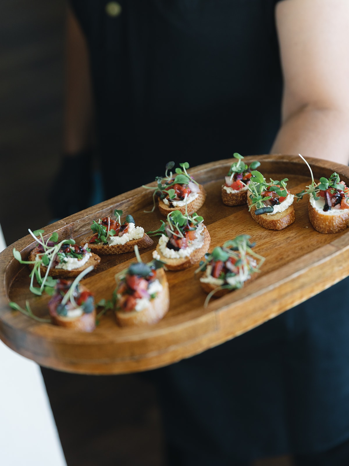 Catered Roots TX server holding a wooden tray of bruschetta appetizers at Corynn and CJ's wedding cocktail hour