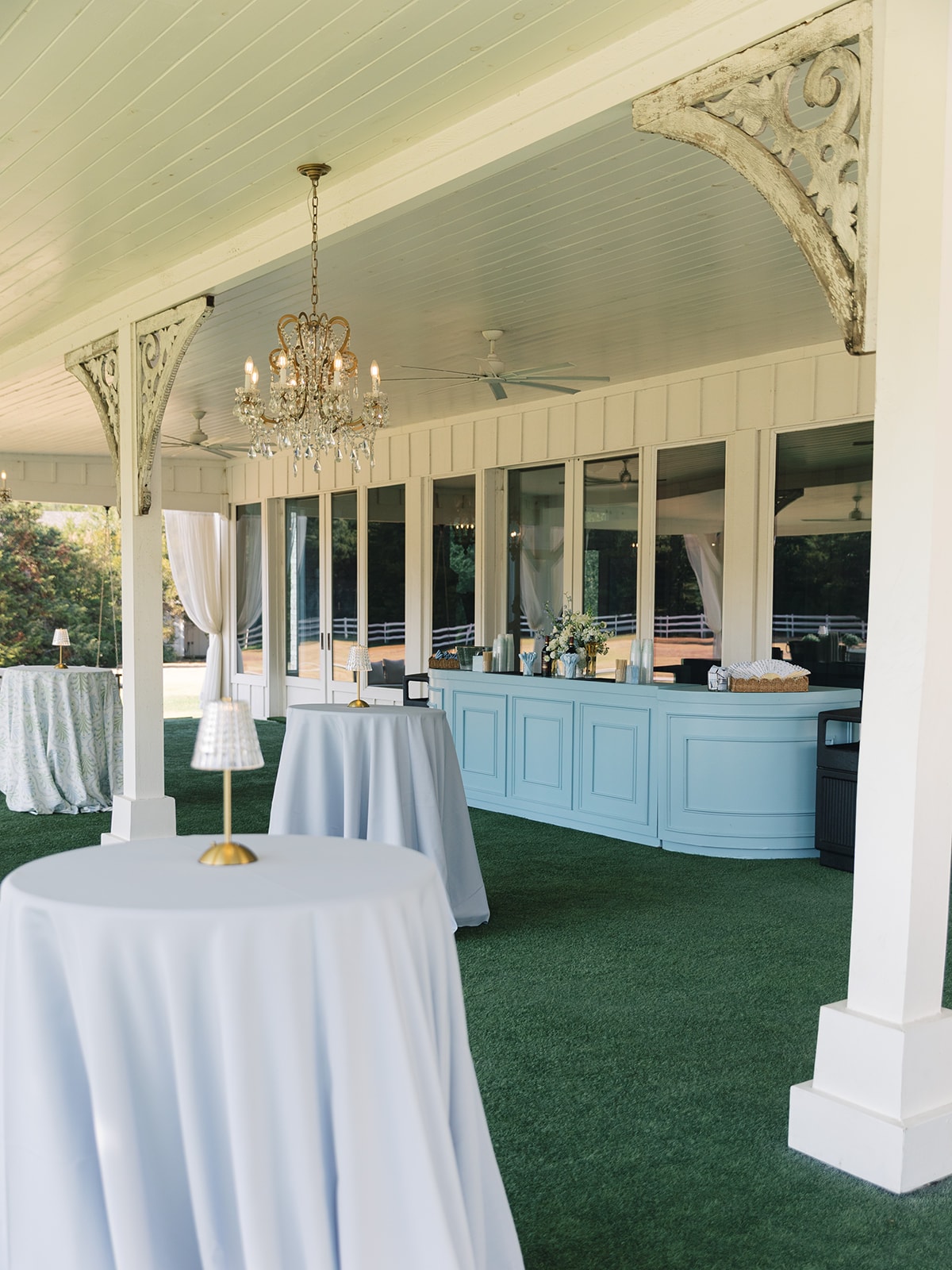 Cocktail hour pavilion at The French Farmhouse Venue with blue bar, crystal chandelier, and white cocktail tables