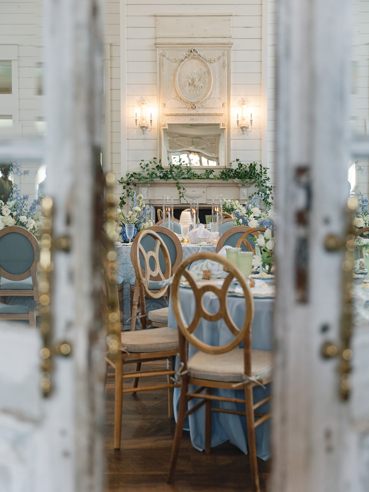 View through the antique French doors into the reception hall with the ornate fireplace and blue and white florals