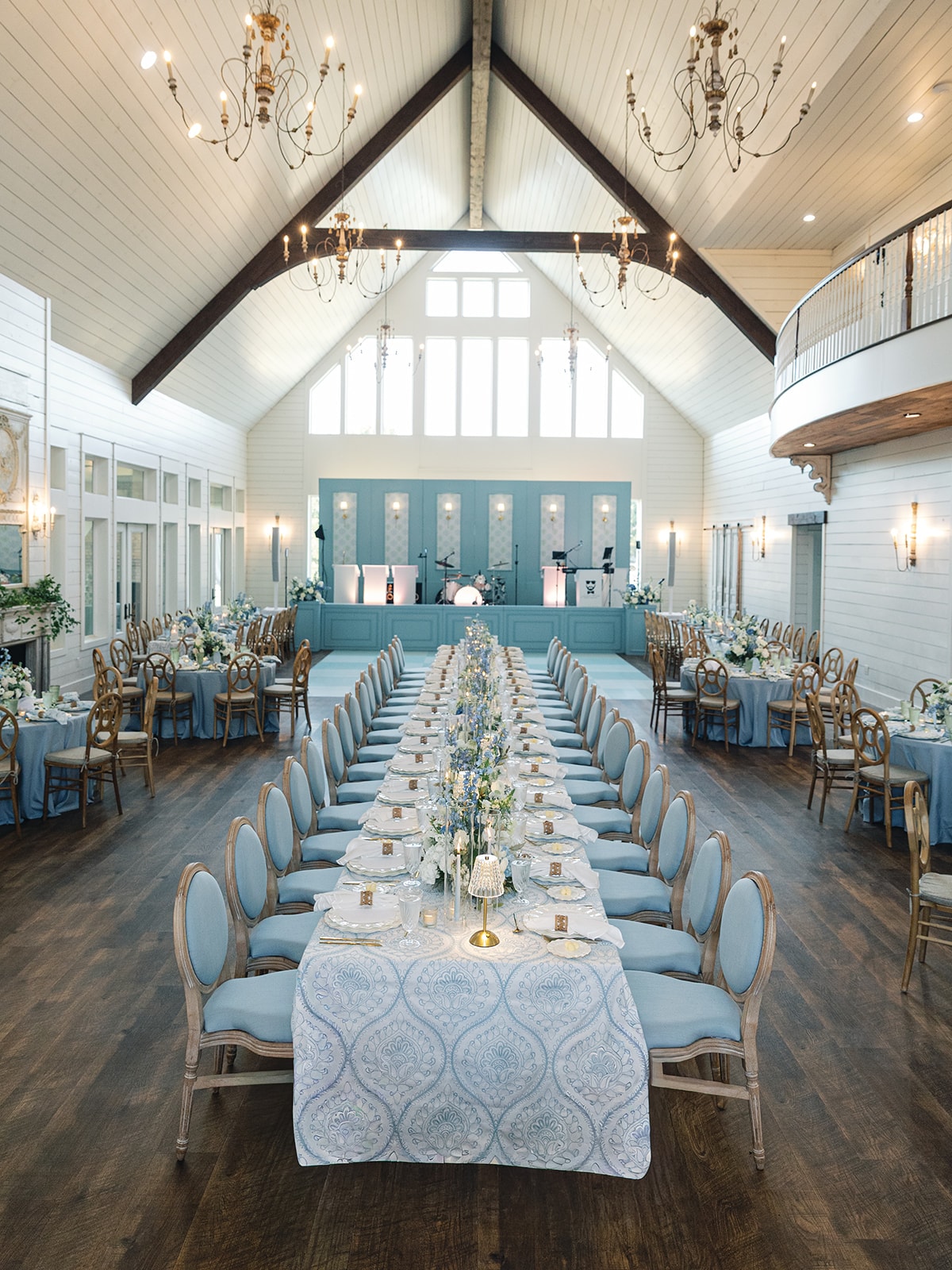 Wide shot of The French Farmhouse Venue reception hall with blue and white tablescapes, chandeliers, and the Jordan Kahn Orchestra stage
