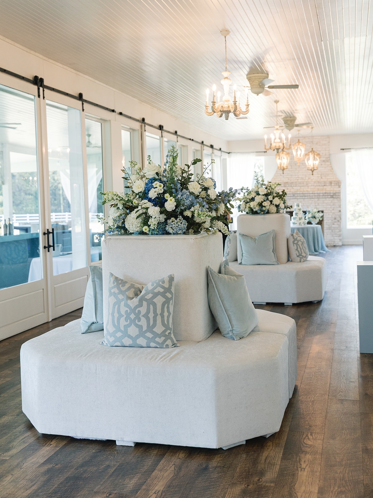 Elegant lounge seating with blue and white floral arrangements and blue accent pillows inside The French Farmhouse reception hall