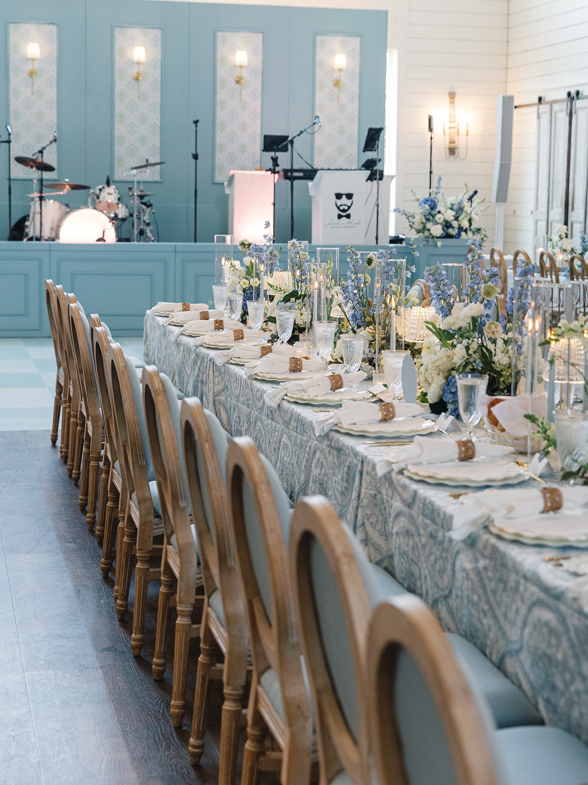 Close-up of the reception tablescape with blue delphinium, white hydrangeas, crystal candlesticks, and gold flatware