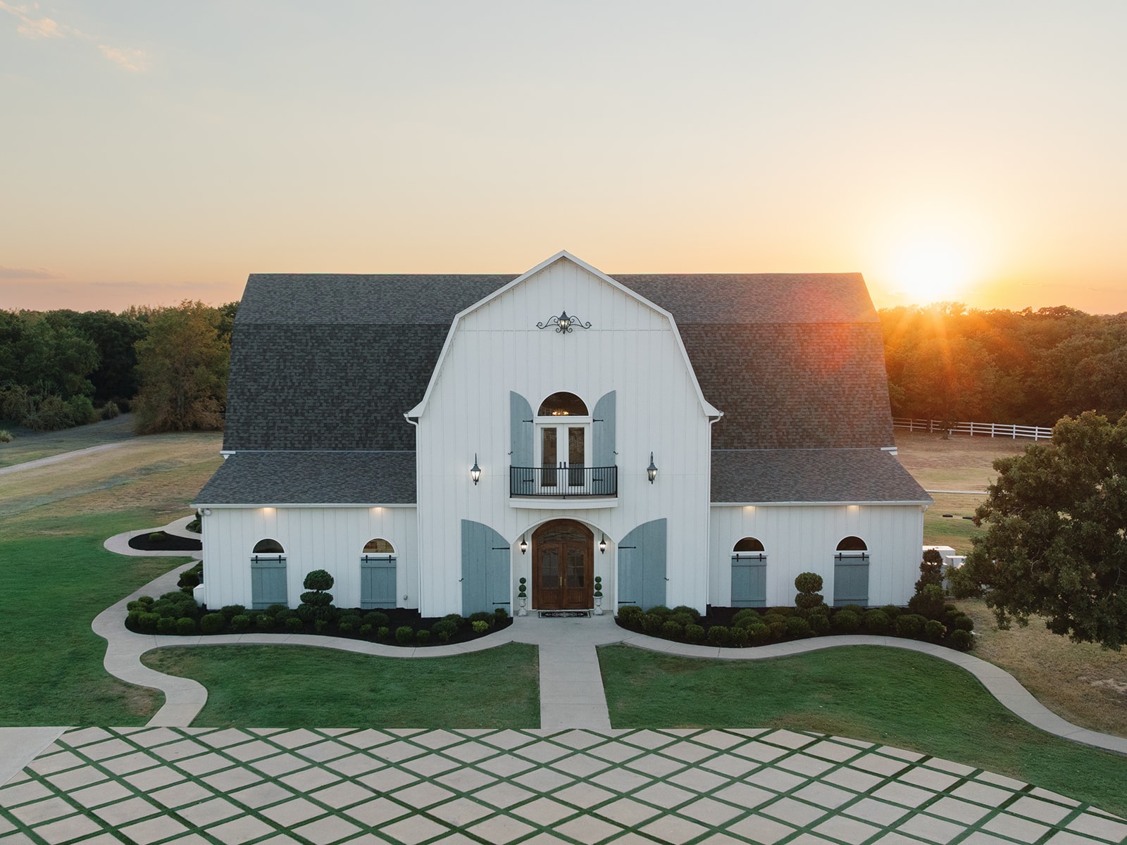 Aerial sunset view of The French Farmhouse Venue exterior with golden hour light and the checkered parking area