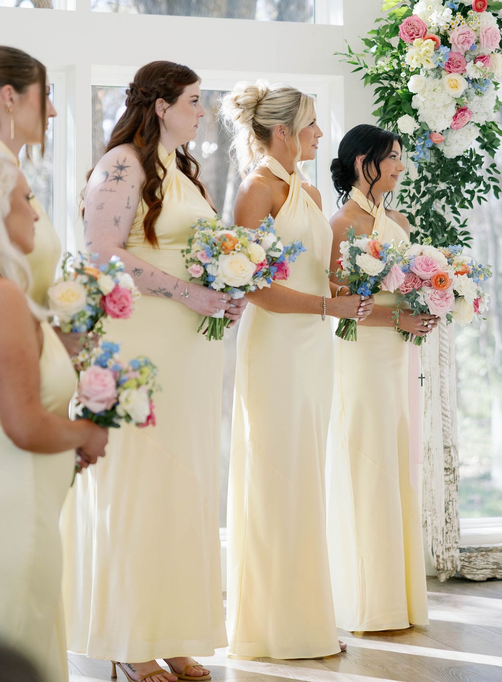 Bridesmaids in butter yellow halter gowns holding colorful bouquets at the chapel altar