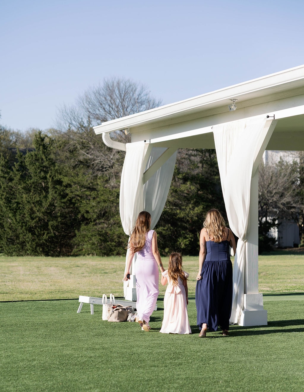 Wedding guests walking toward the white draped pavilion during cocktail hour on a sunny spring afternoon