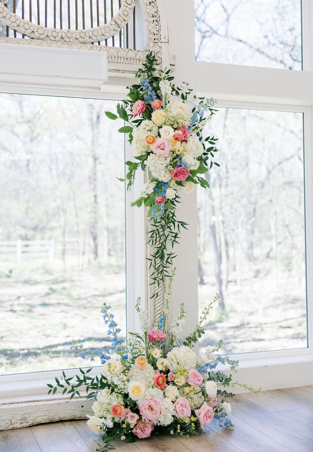 Tall floral column installation with pink, white, and blue blooms against the chapel windows