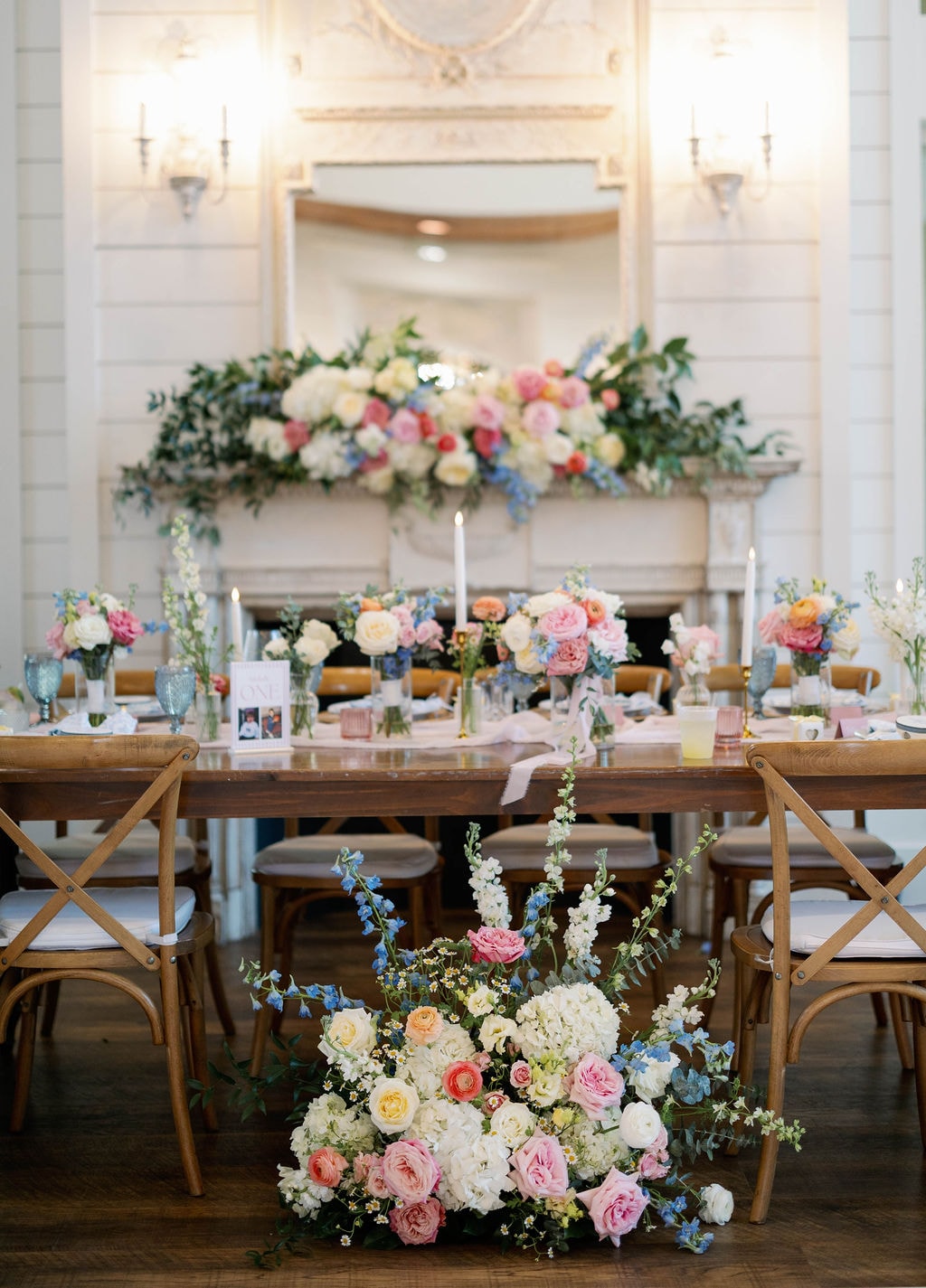 Reception hall with lush floral arrangements on the fireplace mantel and a ground floral installation
