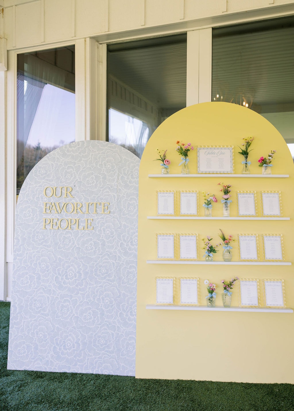 Yellow arch seating chart display reading Our Favorite People with framed table lists and mini florals