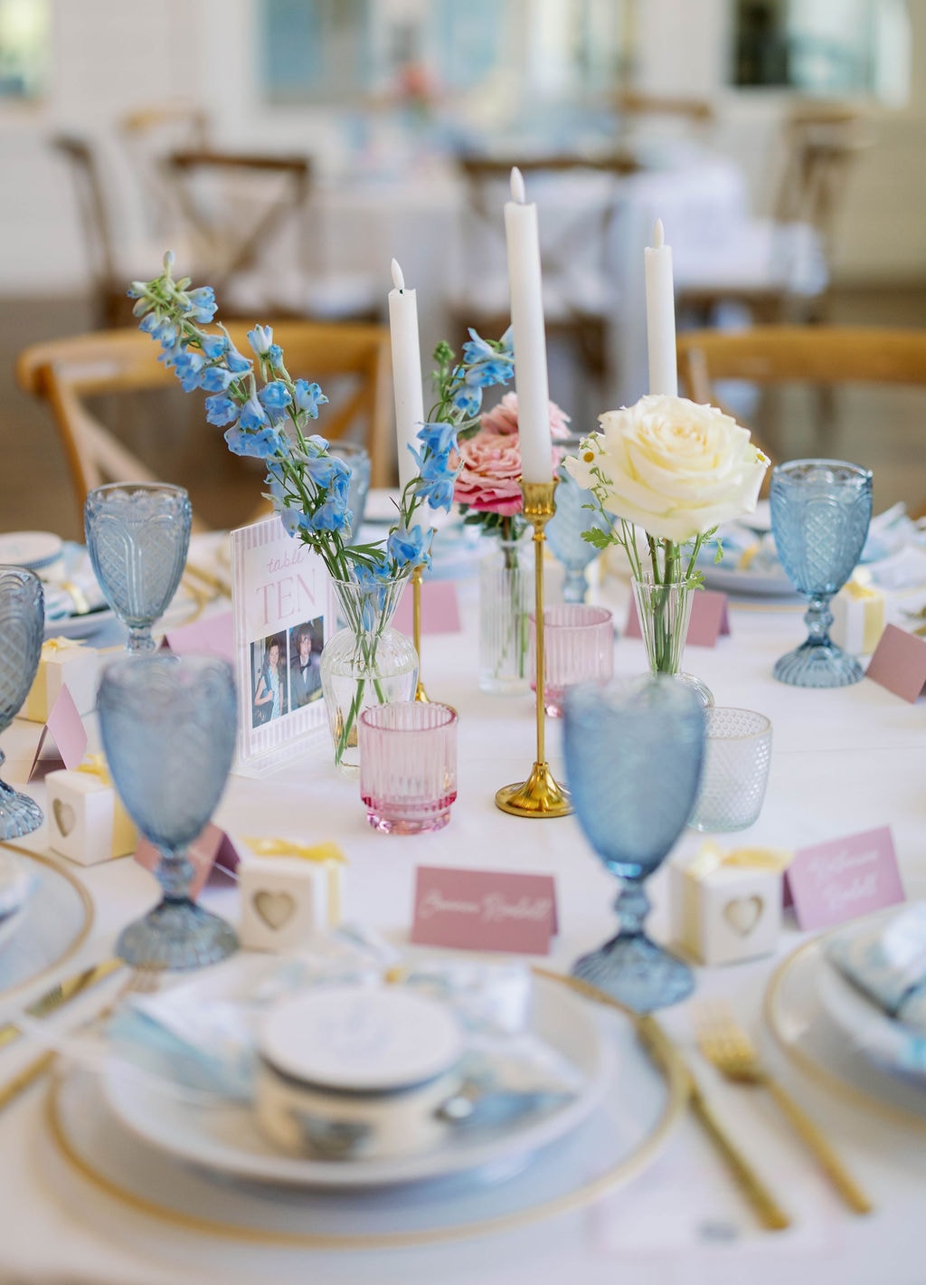 Reception table detail with blue glassware, pink place cards, gold candlesticks, and bud vases