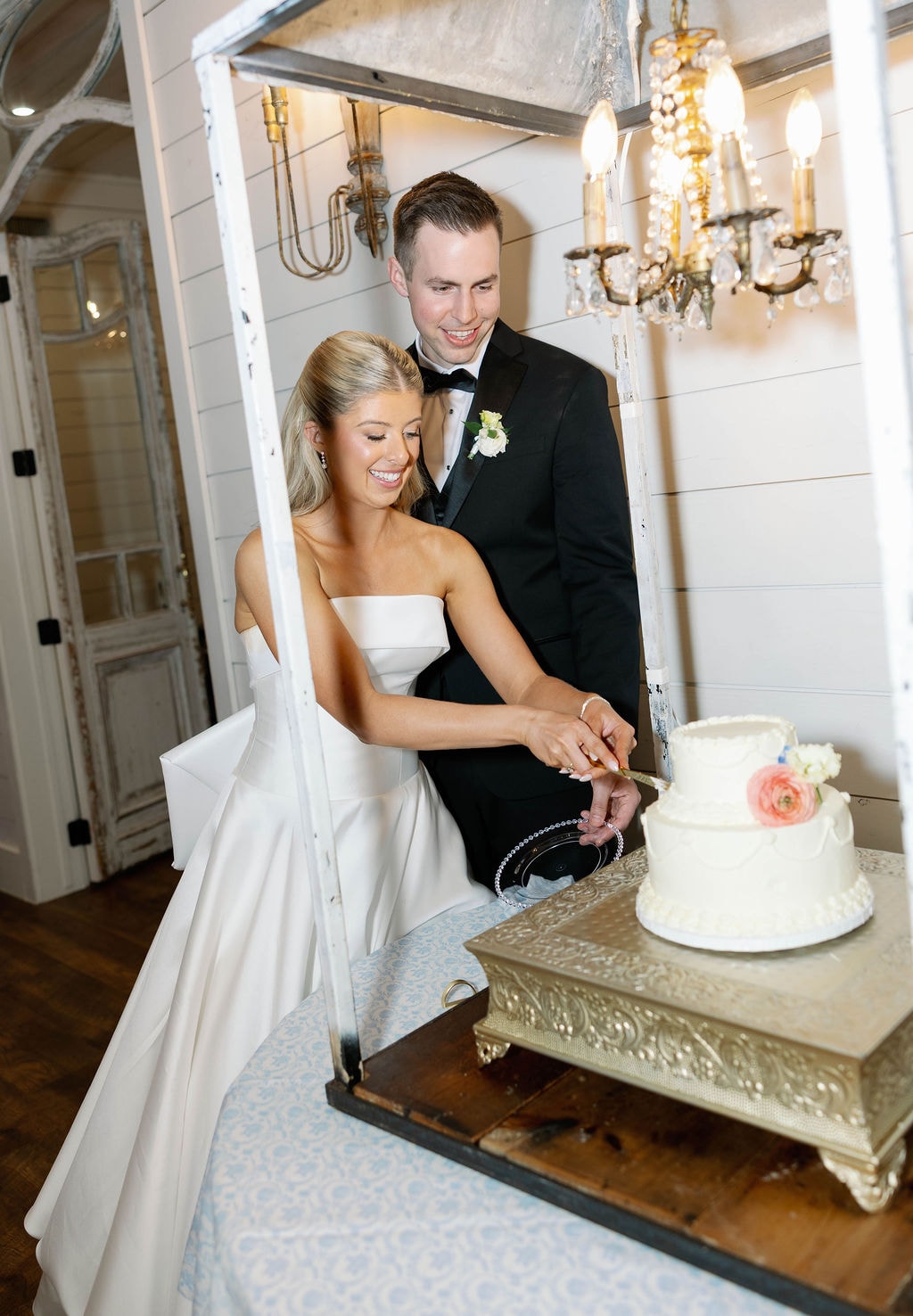 Janie and Jake cutting their wedding cake under a crystal chandelier in the farmhouse