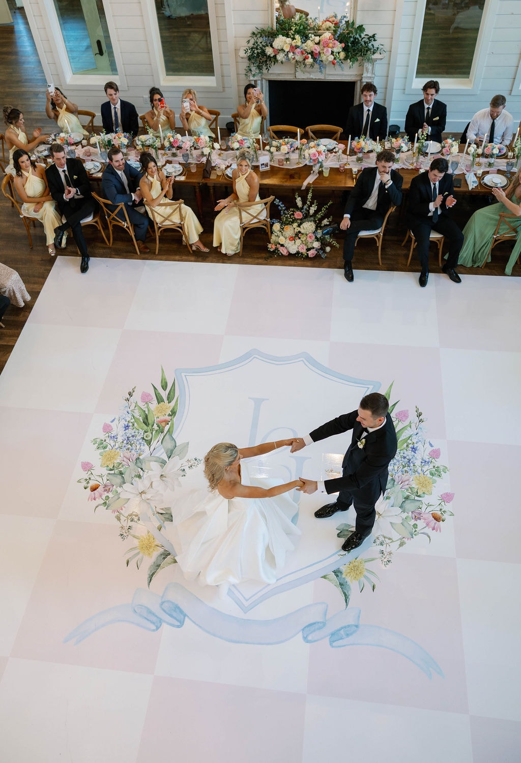 Aerial view of Janie and Jake's first dance on the custom hand-painted floral monogram dance floor surrounded by guests