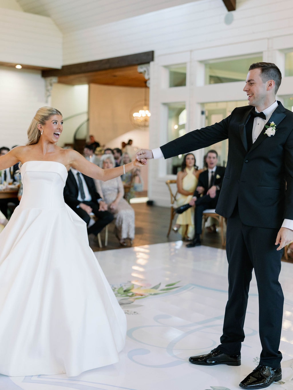Janie laughing as Jake spins her during their first dance, guests cheering in the background