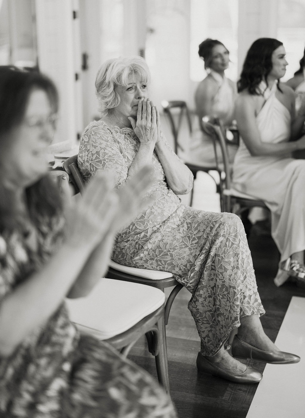 Grandma with hands clasped over her mouth, overcome with emotion watching the surprise grandpa dance, in black and white