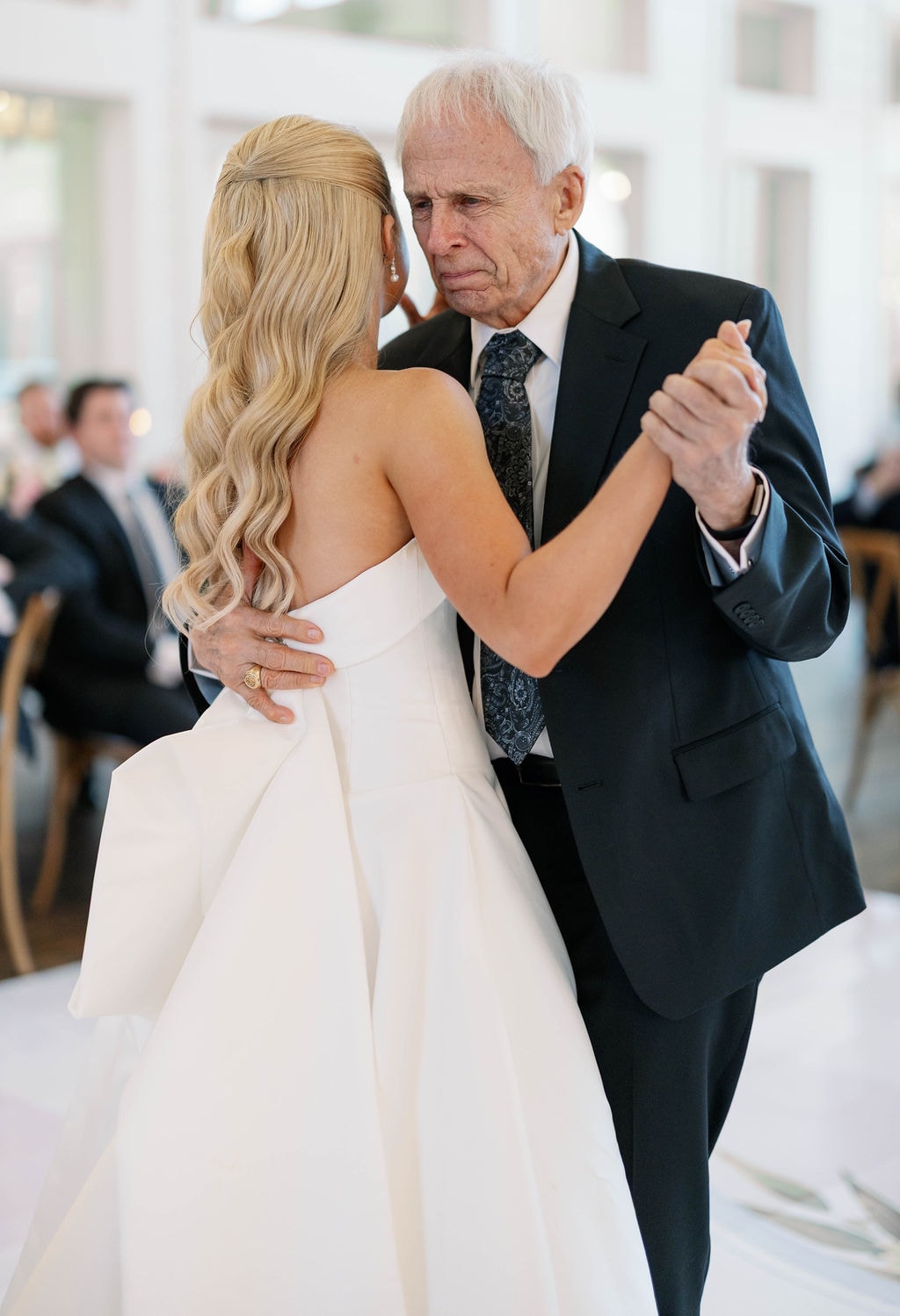 Wide shot of Janie and her grandpa dancing together on the reception dance floor surrounded by family watching