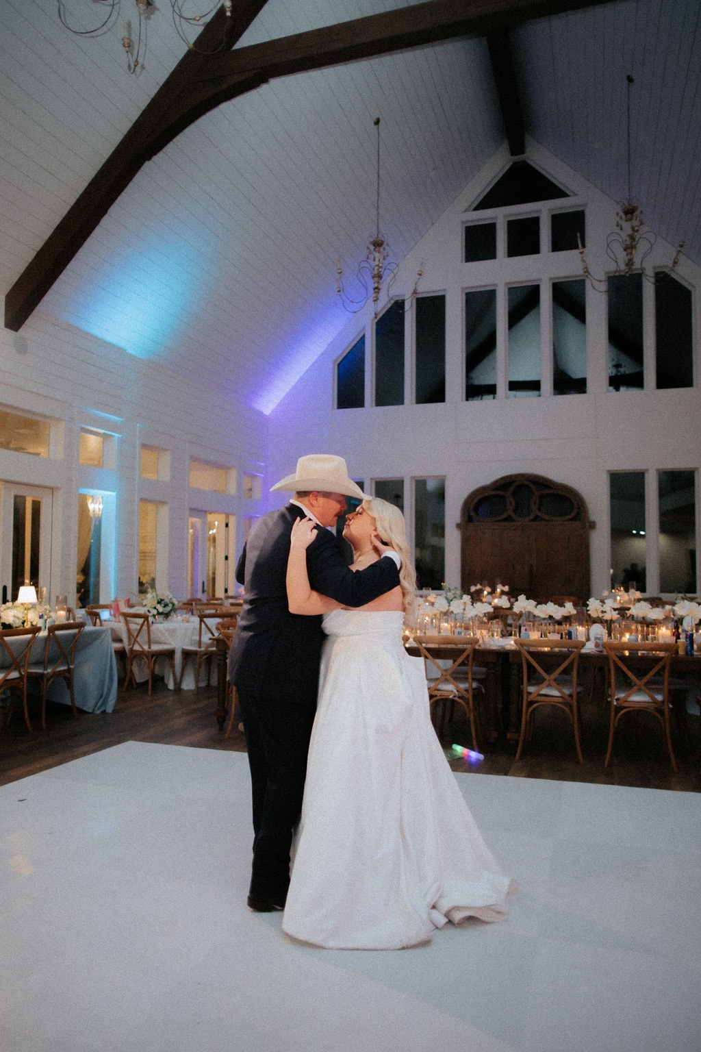 Kara and Anthony sharing their first dance on the white dance floor with blue uplighting glowing across the soaring cathedral ceiling