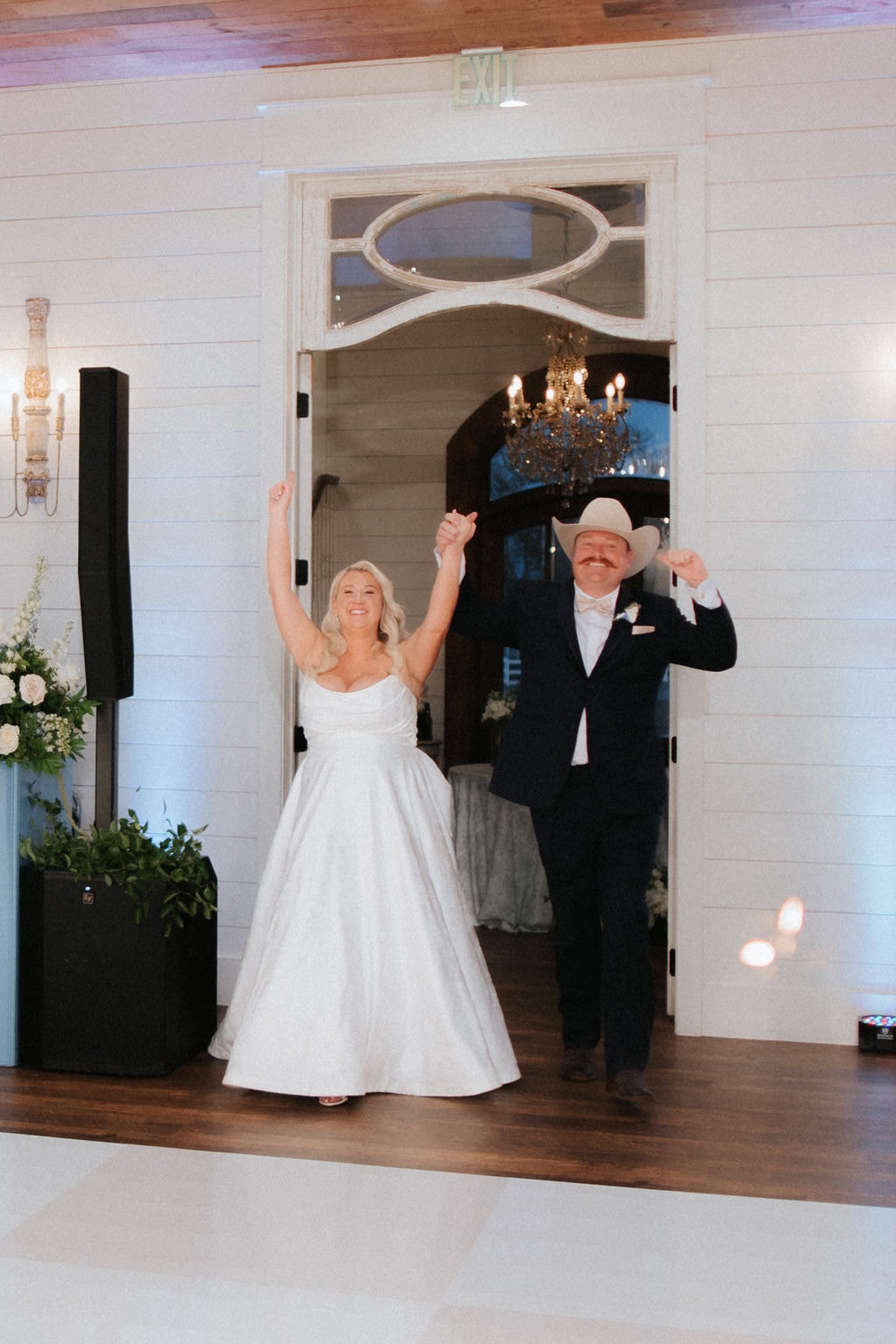 Kara and Anthony Marquardt making their grand entrance into the reception hall at The French Farmhouse Venue — both with hands raised and huge smiles, guests cheering behind them