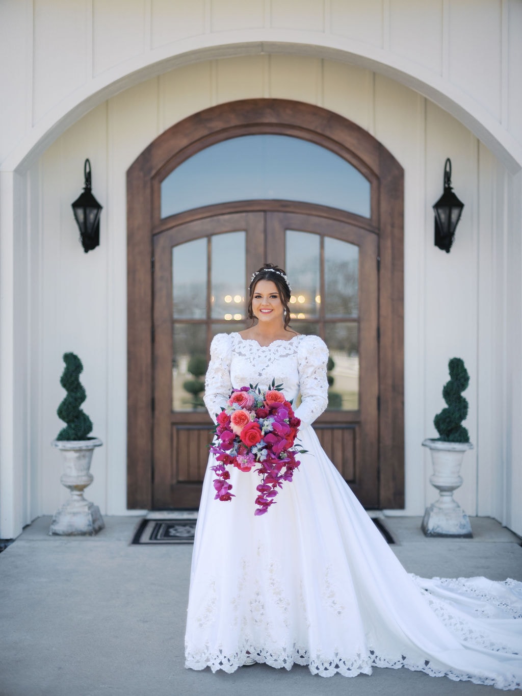 Katherine standing in front of the venue entrance in her lace gown with vibrant bouquet
