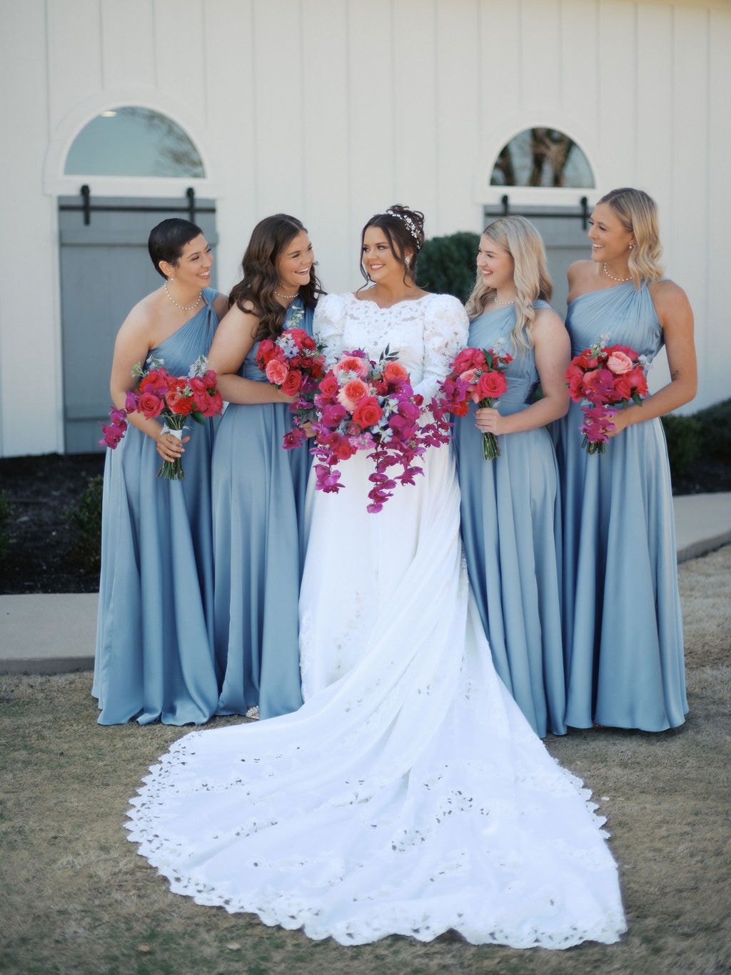 Katherine with her bridesmaids in dusty blue dresses holding pink and fuchsia bouquets