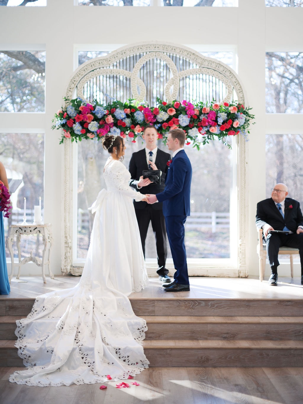 Katherine and Hayden exchanging vows at the antique arch with colorful floral arrangement