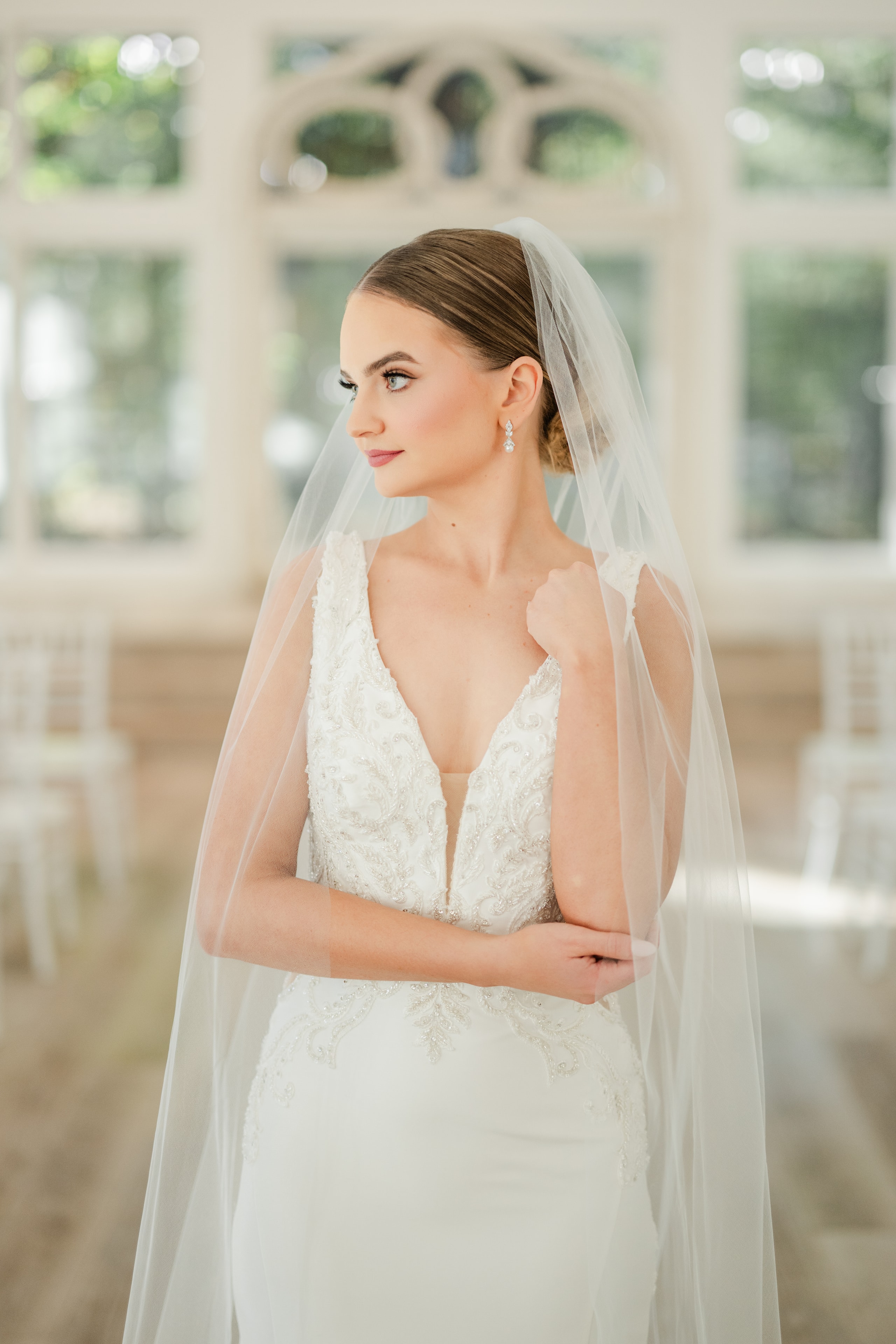 Bridal portrait inside The French Farmhouse reception hall — bride in a beaded lace V-neck gown with cathedral veil, soft light streaming through the arched windows