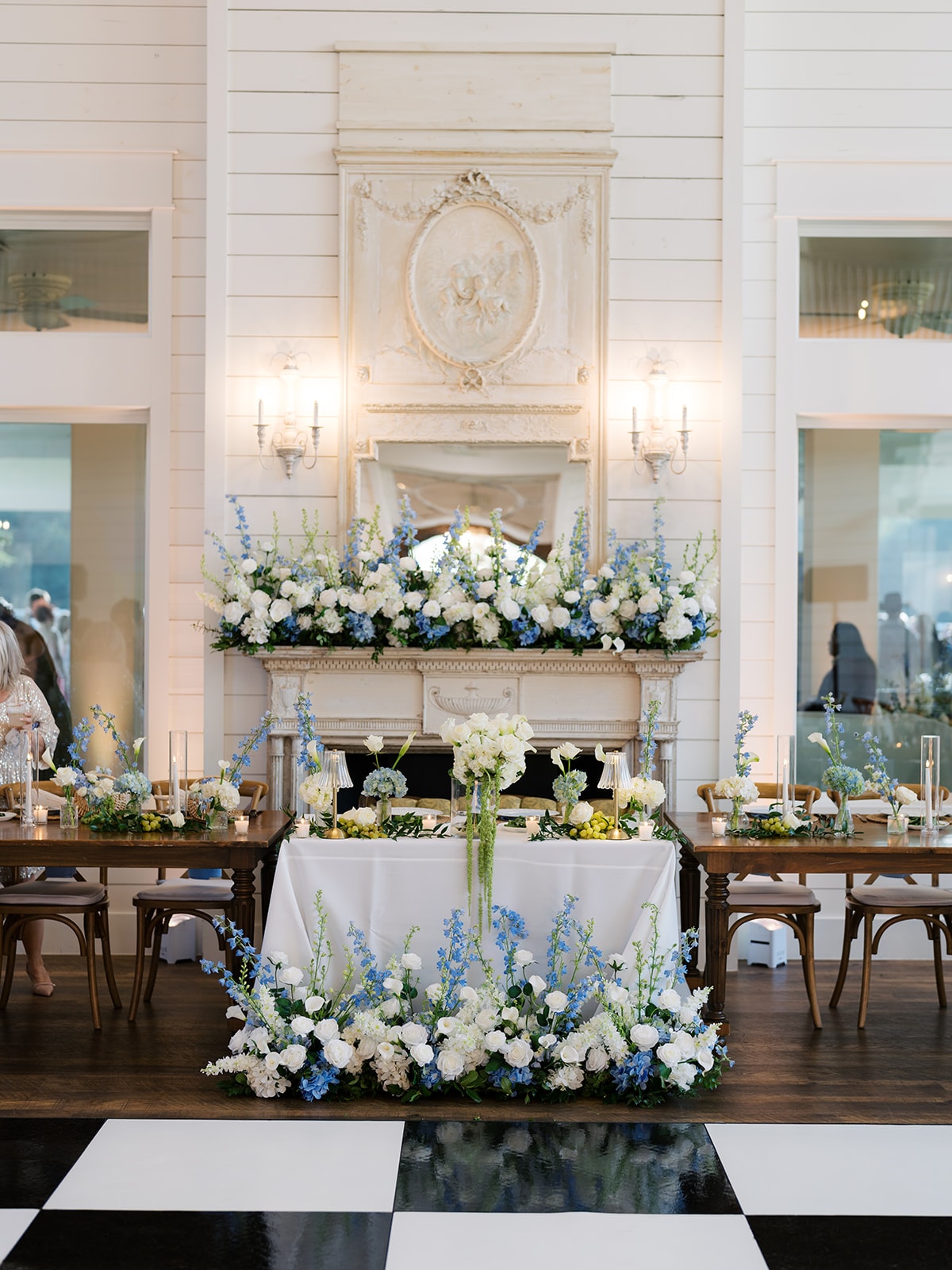 Macey and Brendan's sweetheart table dressed in white linen with an overflowing lush white and greenery floral arrangement cascading across the table, gold candlesticks, and white taper candles
