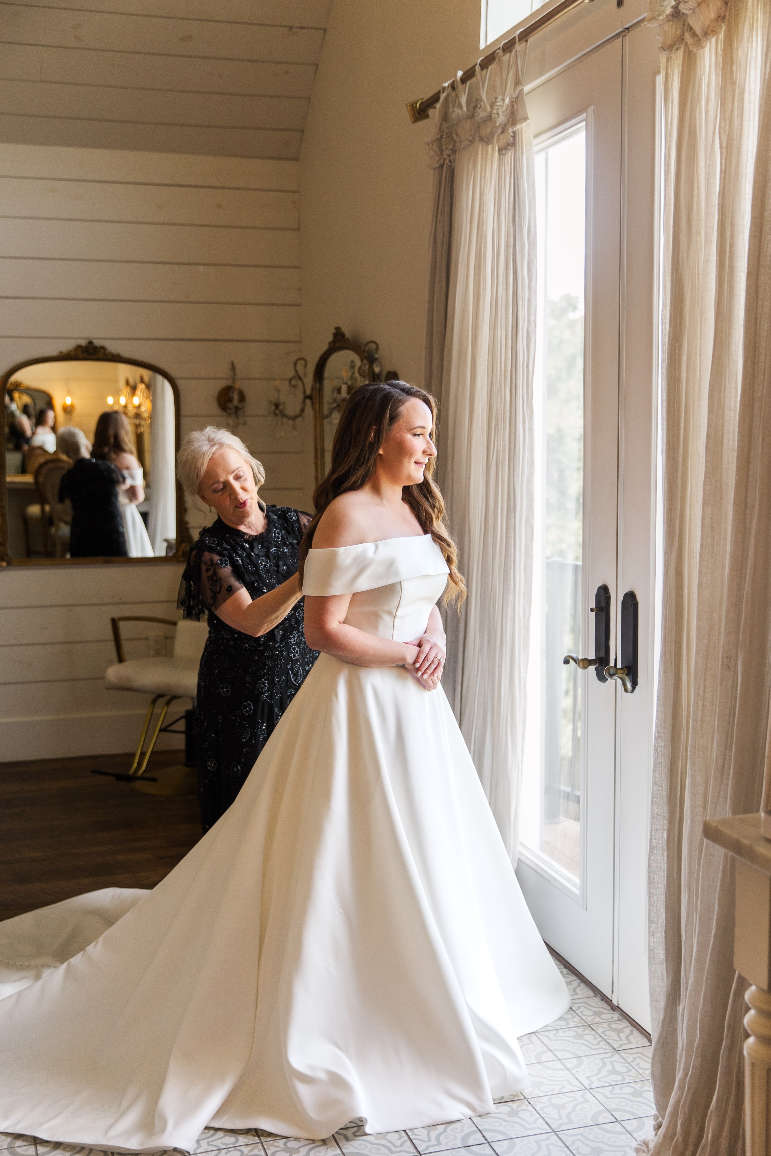 Meaghan's mother helping her into her off-the-shoulder white ballgown in the French Farmhouse bridal suite
