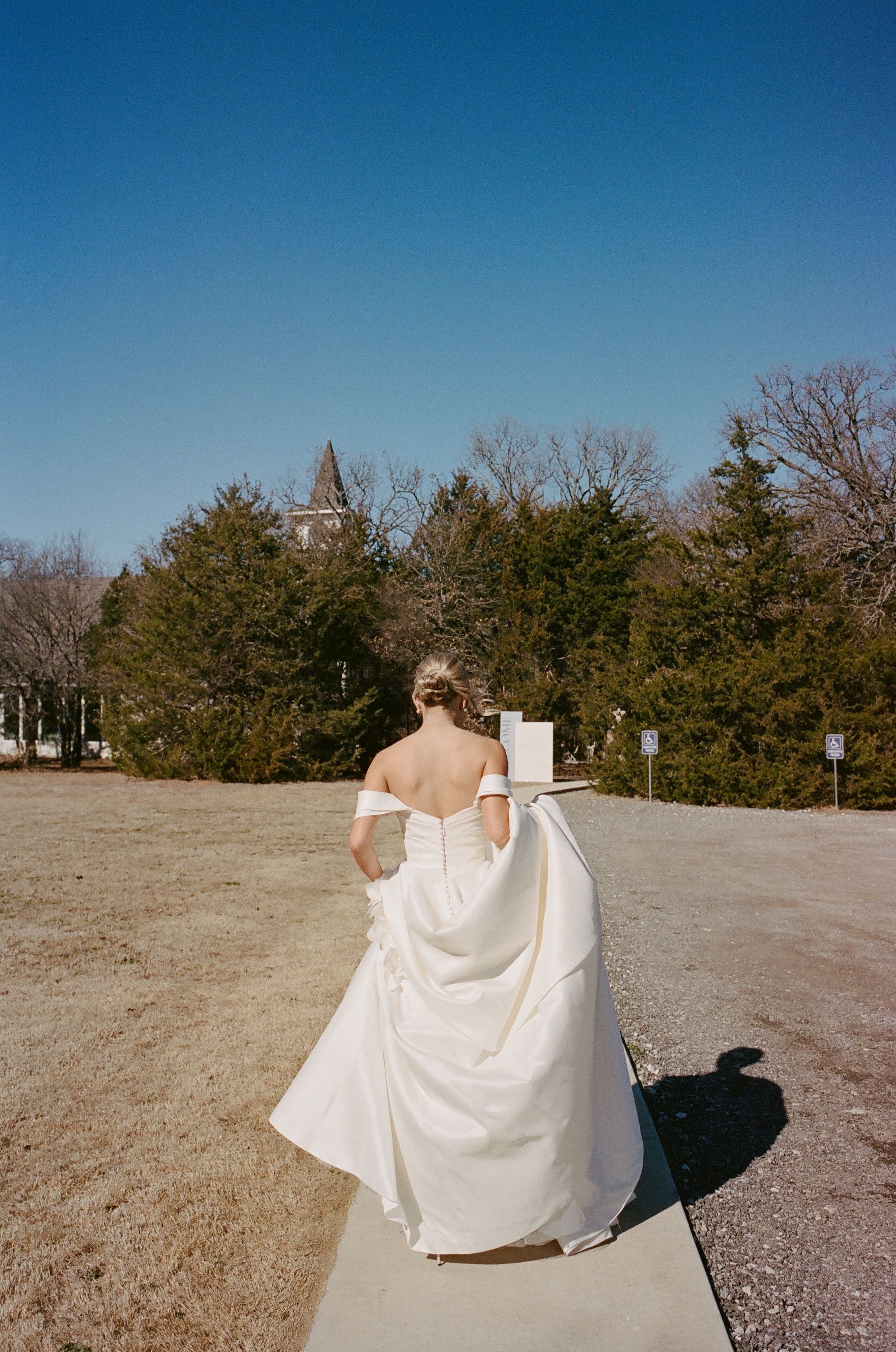 Megan walking toward the chapel from behind in her off-the-shoulder gown under a bright blue winter sky