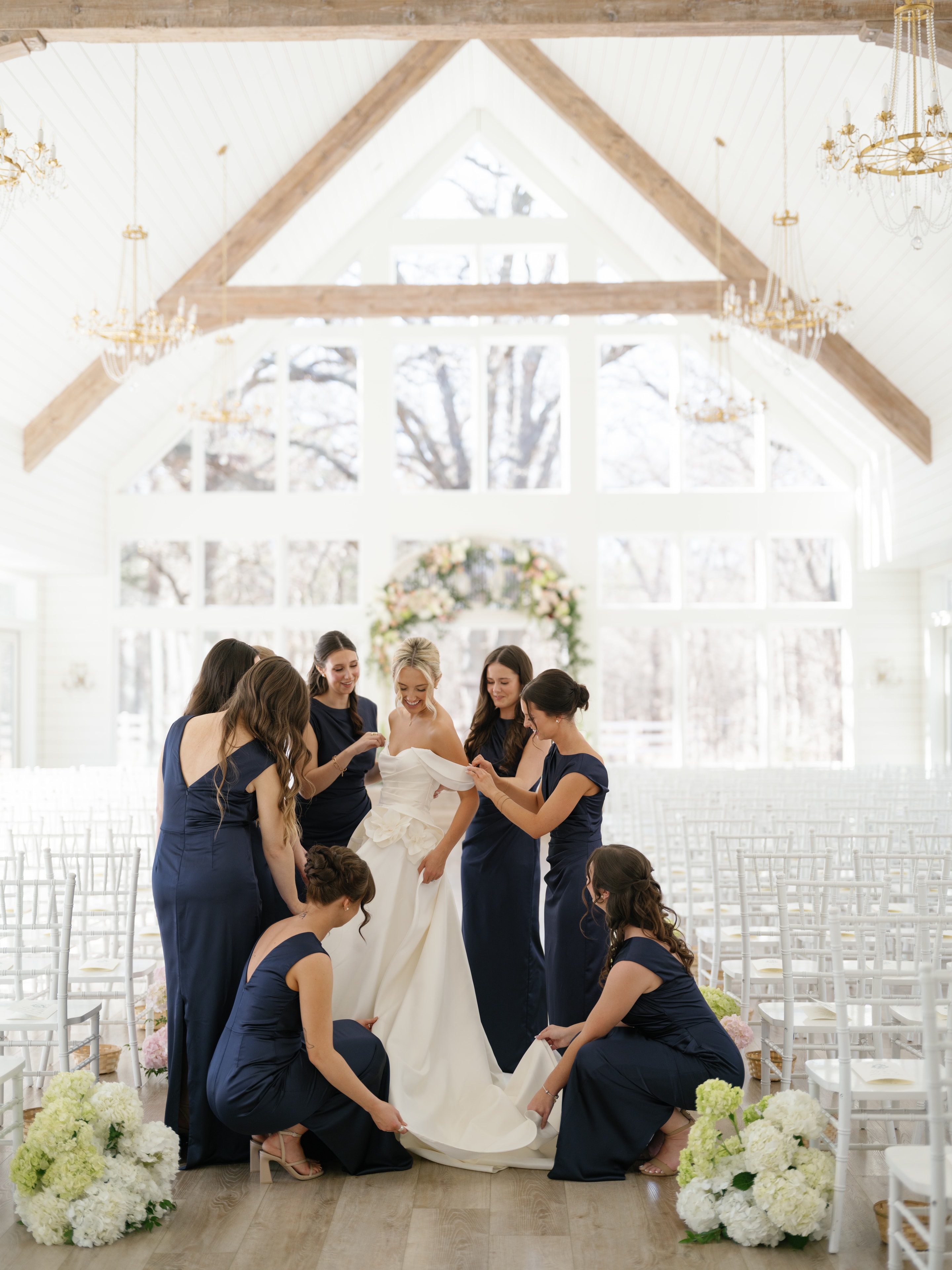 Bridesmaids in navy dresses helping Megan with her gown inside the French Farmhouse chapel