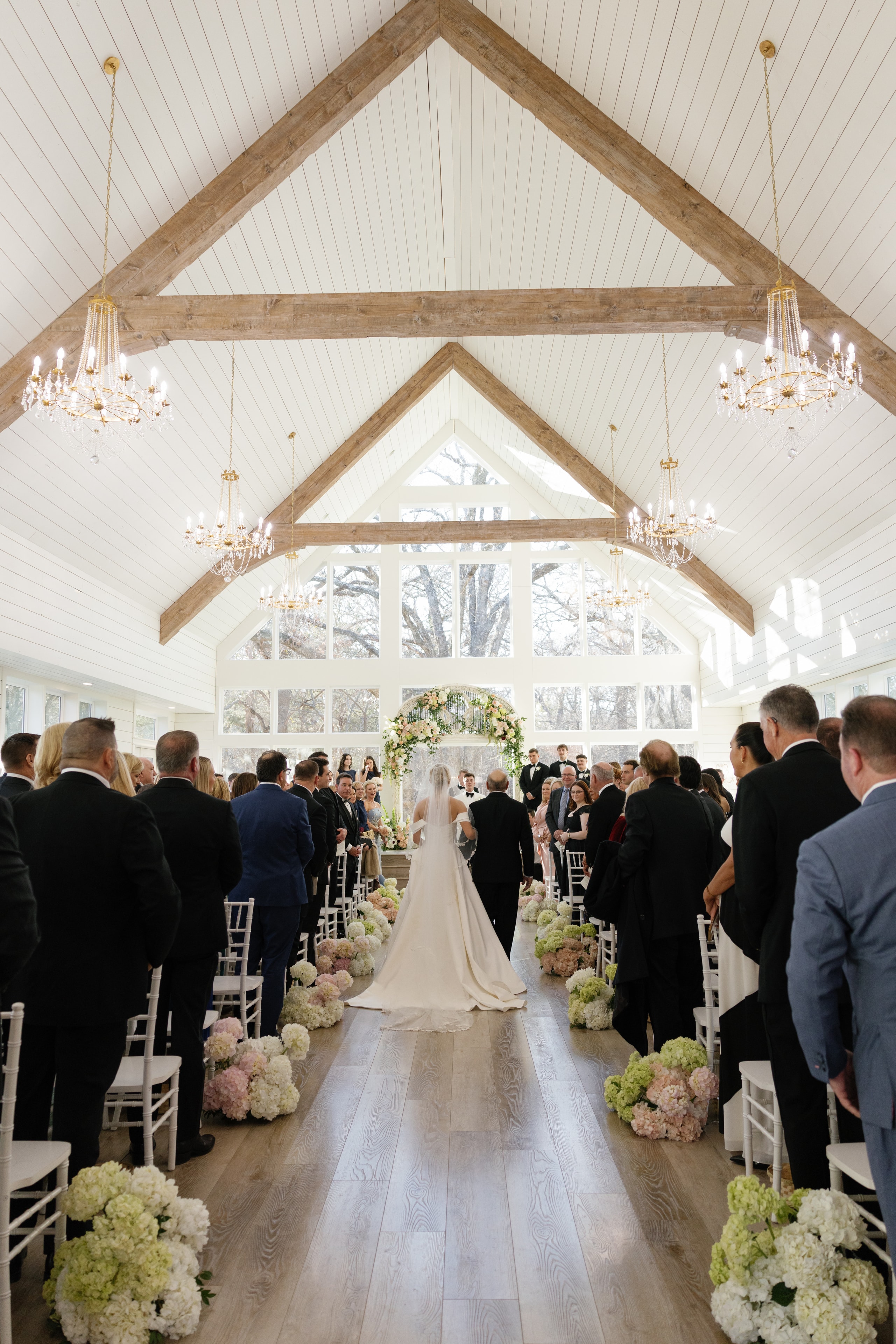 Wide shot of the full French Farmhouse chapel during Megan and Rex's ceremony with soaring ceilings and hydrangea aisle flowers