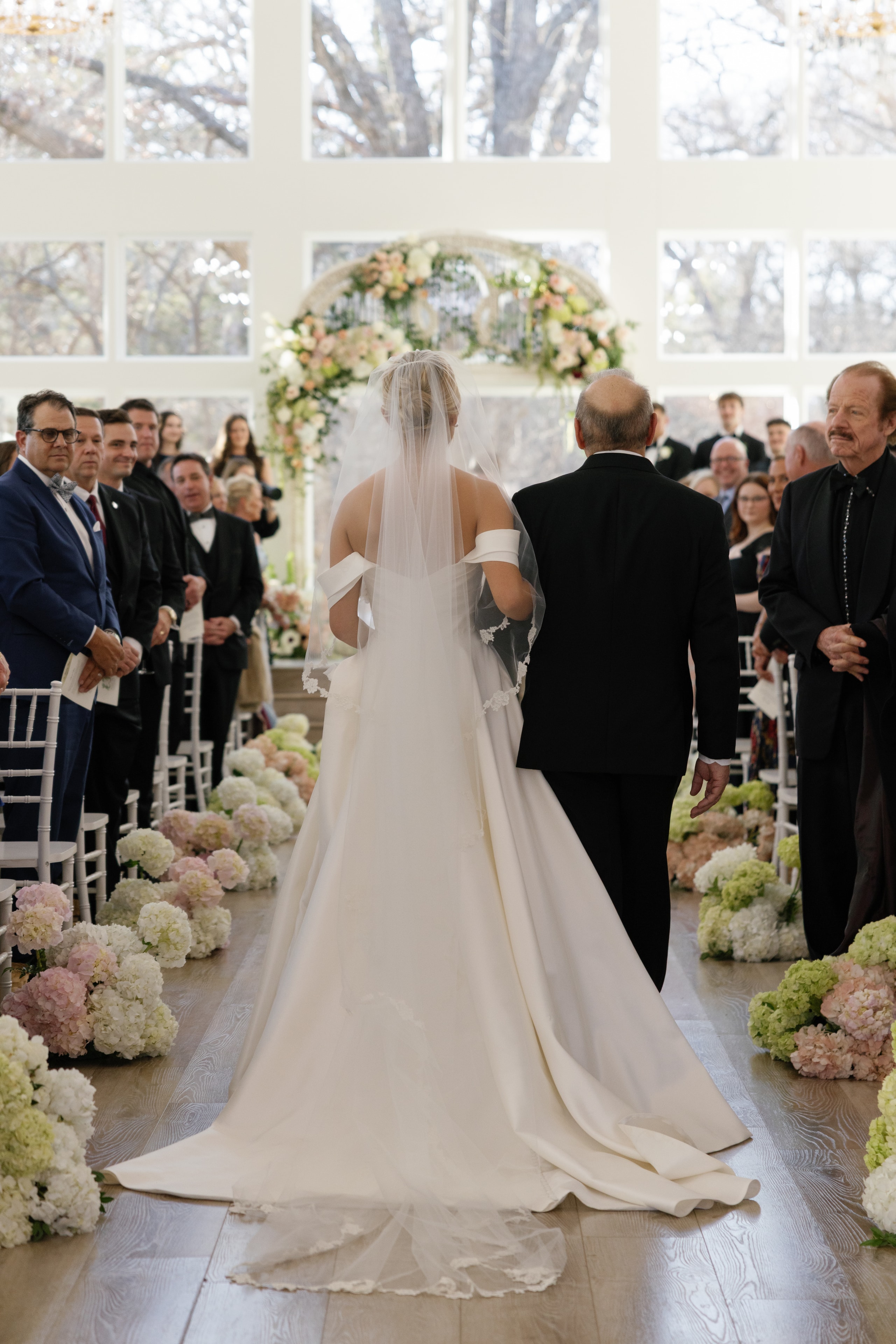 Close-up of Megan walking down the aisle with her father past seated guests at The French Farmhouse chapel