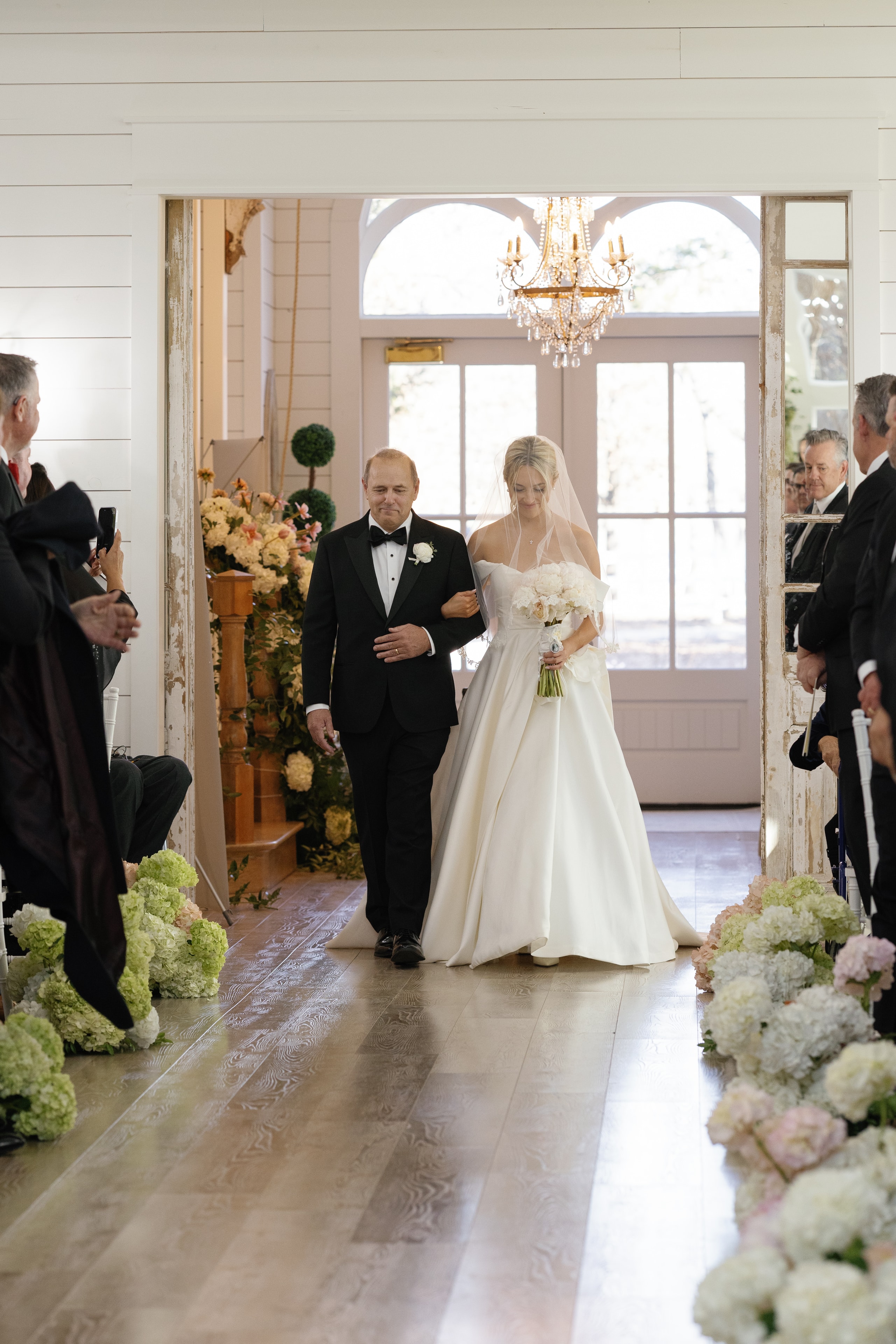 Megan walking down the aisle with her father from behind showing her cathedral veil and train