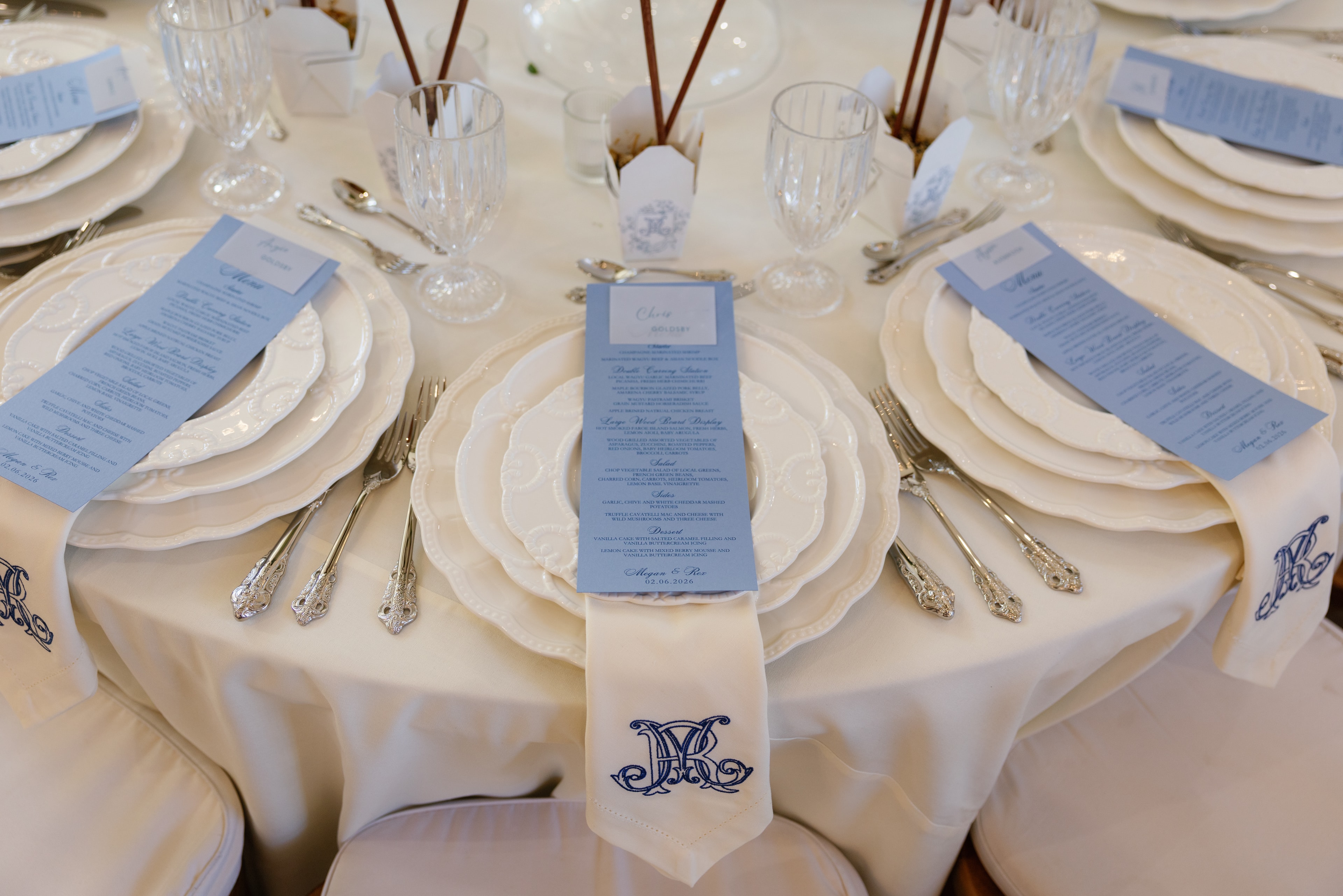 Elegant blue and ivory place setting with monogrammed napkin and menu card reading Megan and Rex 02.06.2026
