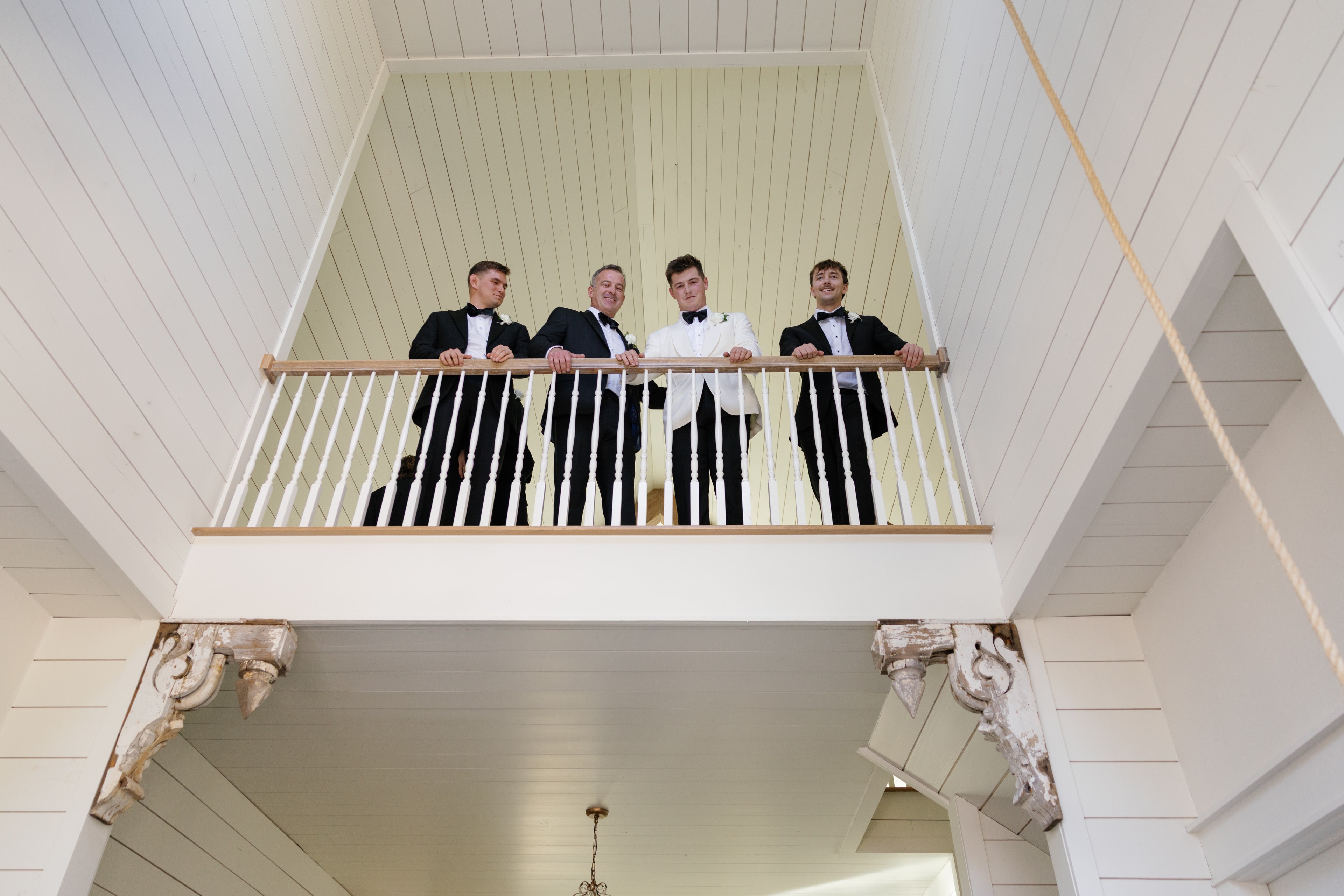 Rex and groomsmen in tuxedos leaning over the balcony railing at The French Farmhouse Venue