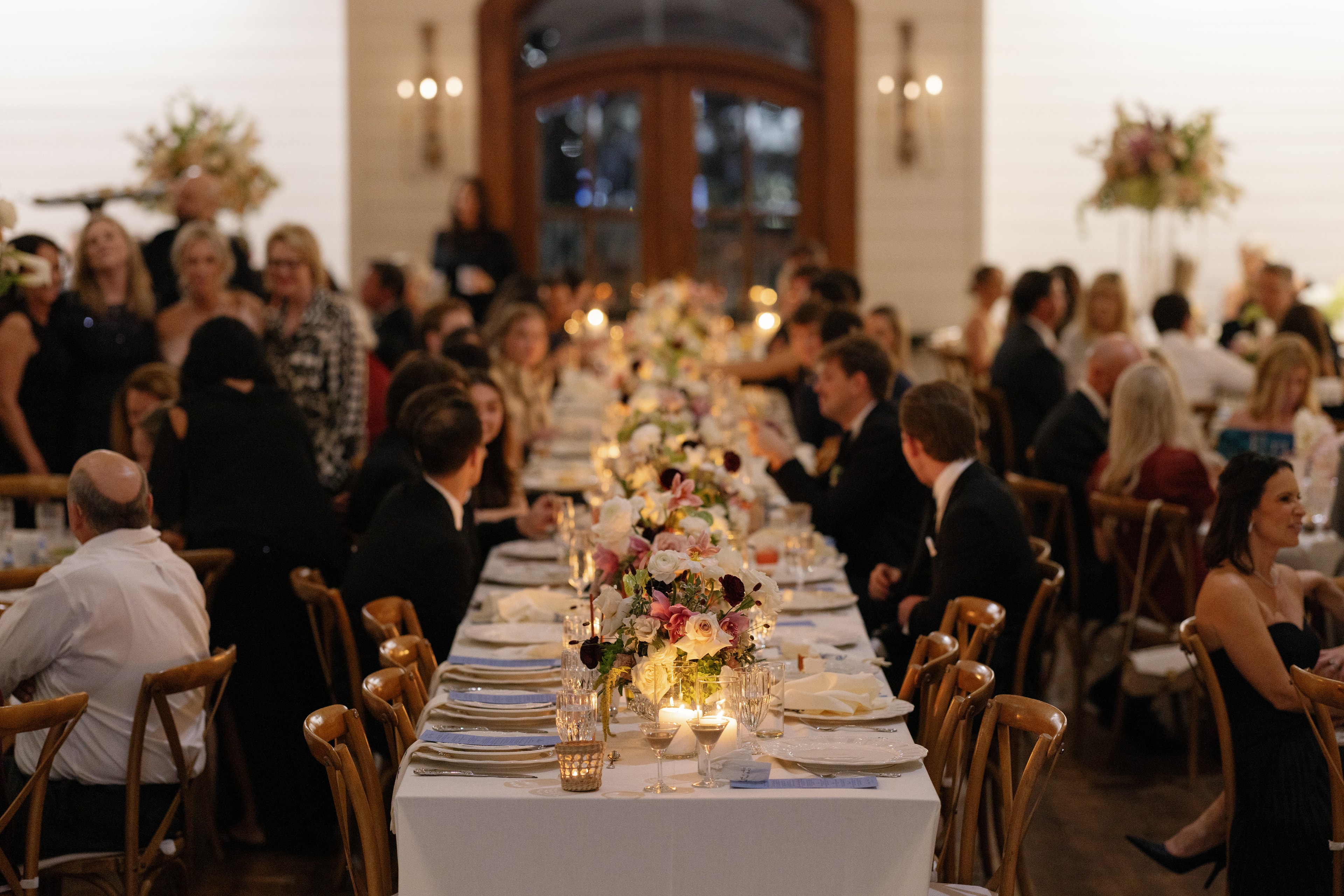 Long farm table filled with guests and lush floral centerpieces at the Megan and Rex reception dinner