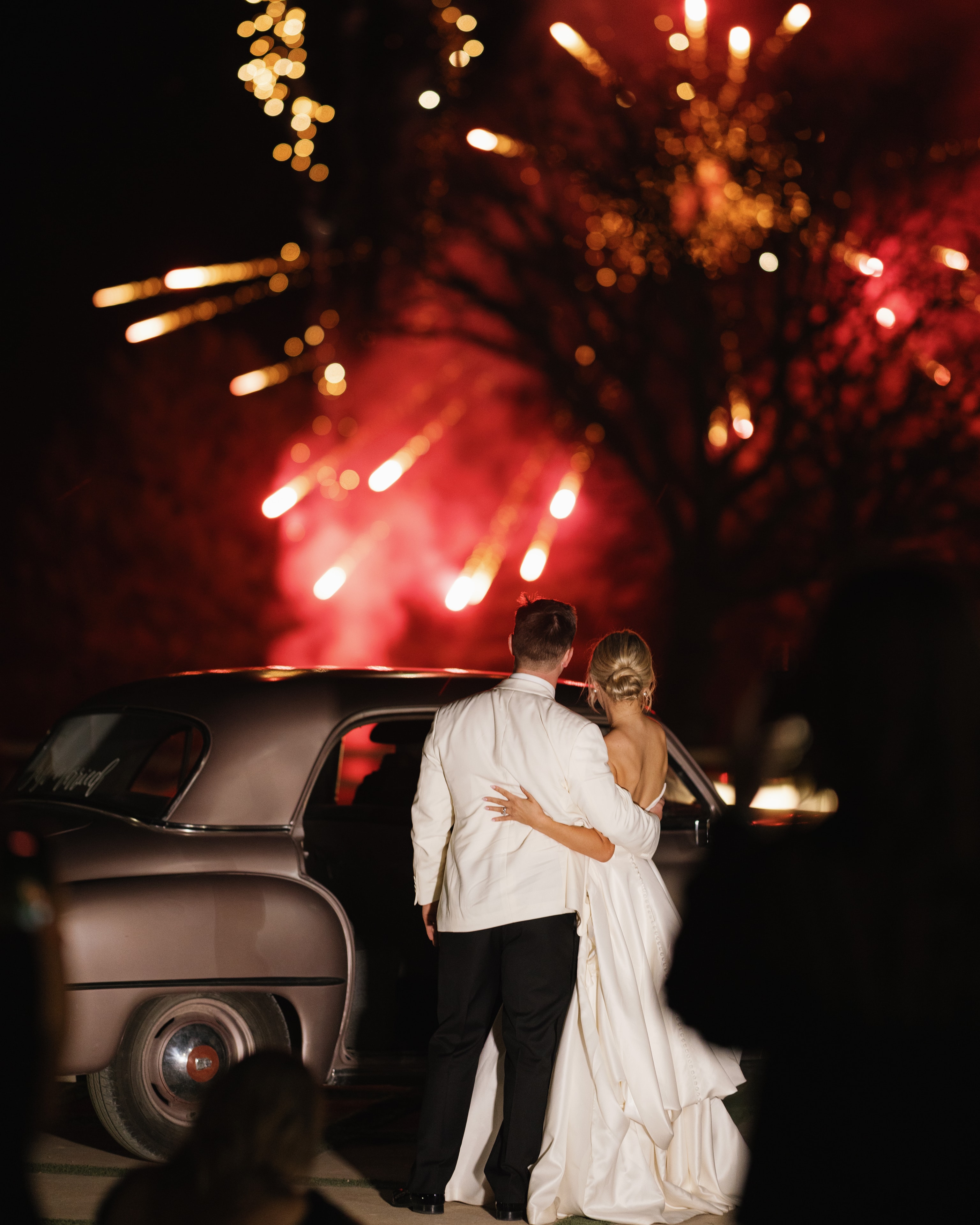 Megan and Rex watching fireworks burst overhead beside their vintage getaway car at The French Farmhouse Venue