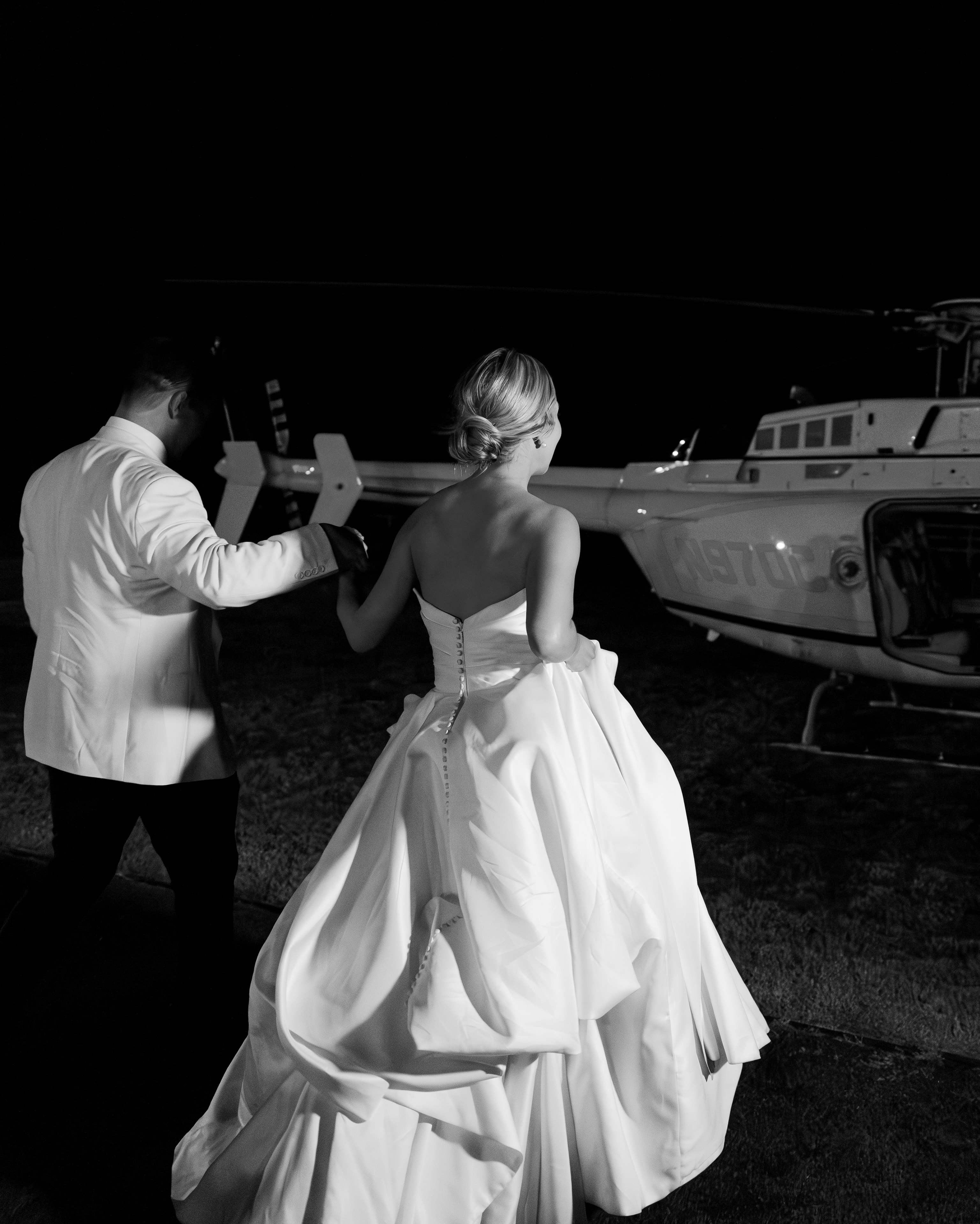 Black and white photo of Megan and Rex walking hand in hand toward the Longhorn helicopter for their wedding exit