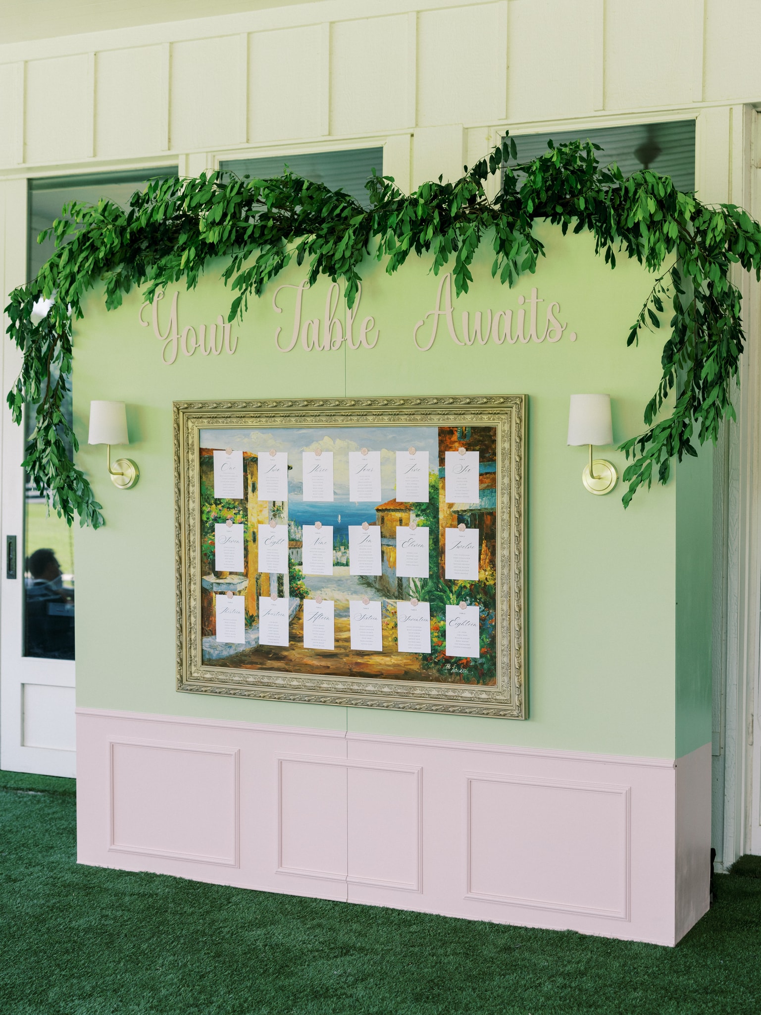Morgan and Jack's custom seating chart — an elegant hand-lettered display board with gold calligraphy listing guest table assignments, surrounded by blush florals