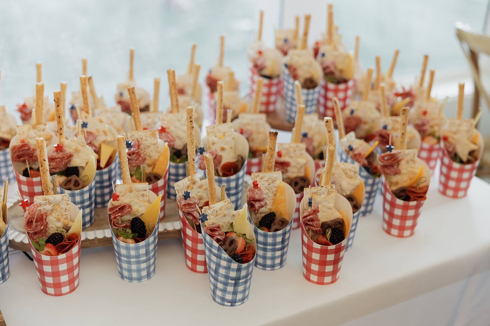 Louie Boards and Co. individual charcuterie cones in red and blue gingham cups with salami, cheese, berries, and breadsticks for Nina and Gage's 4th of July cocktail hour
