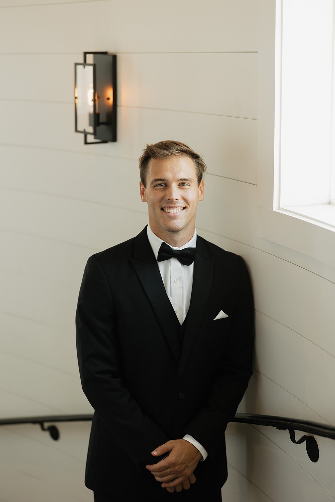 Gage Jackson in his black tuxedo and bow tie on the groom's room staircase at The French Farmhouse Venue on his wedding day