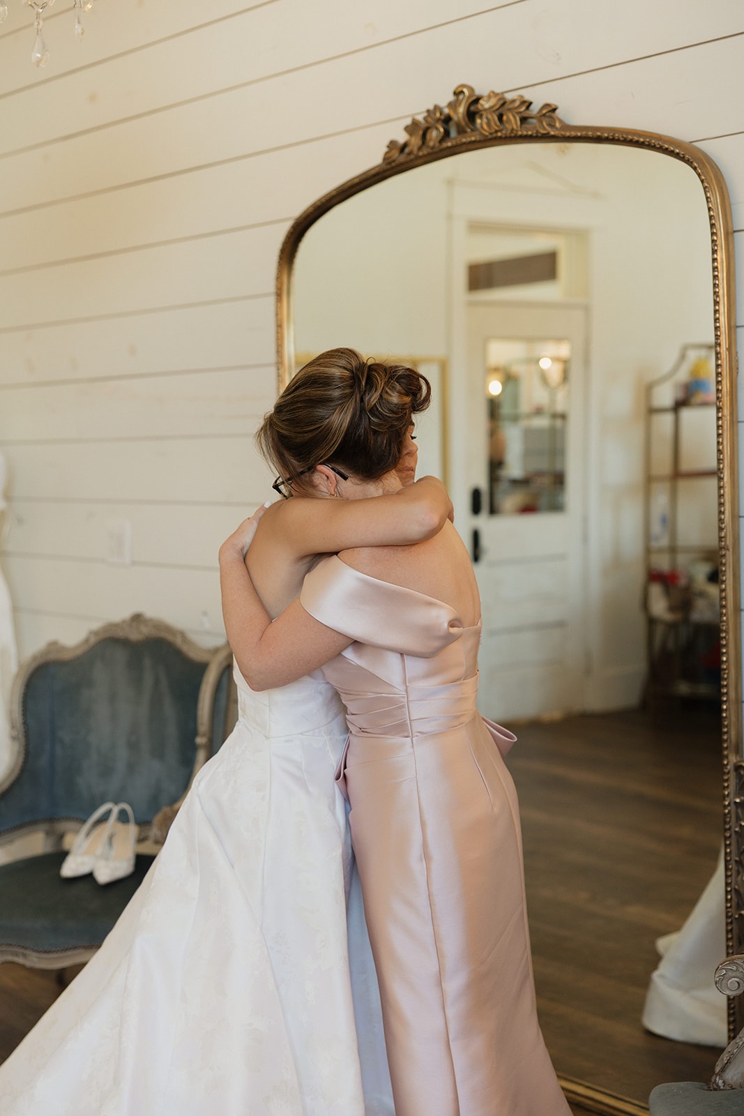 Nina and her mom Amy sharing a heartfelt embrace in front of the gold mirror in the bridal suite at The French Farmhouse Venue on the morning of her 4th of July wedding