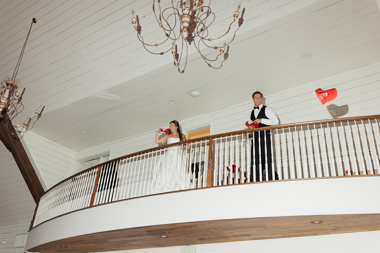 Nina and Gage watching a burst of colorful red, blue, and gold fireworks by Dallas Elevate light up the night sky at The French Farmhouse Venue — white fence glowing in the background