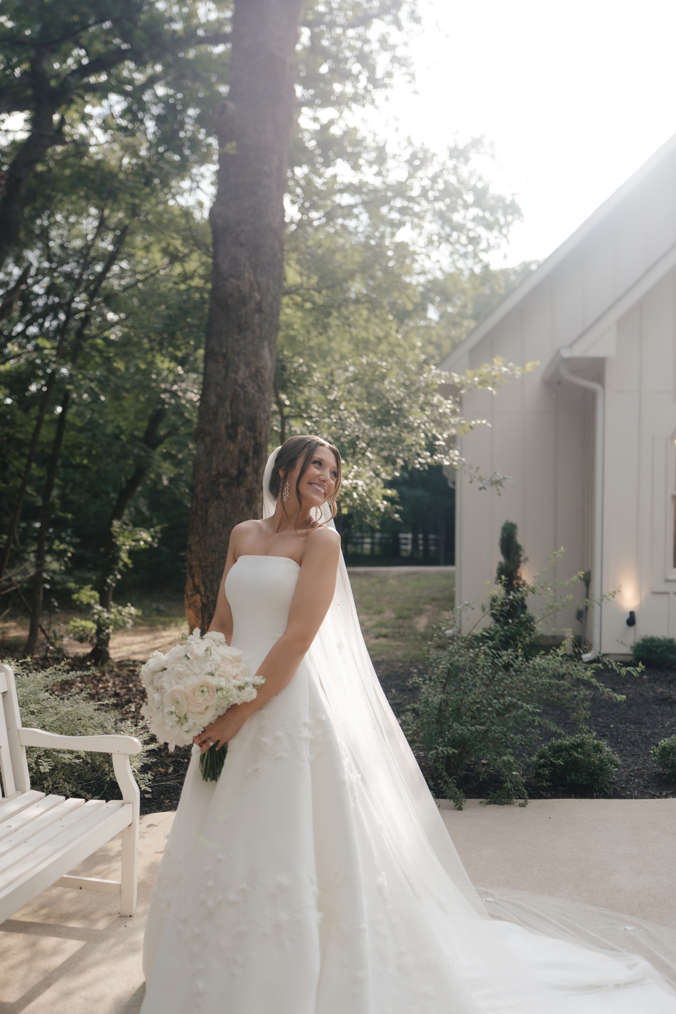 Paige in her strapless white gown with cathedral veil holding a white and blush bouquet outside The French Farmhouse Venue chapel