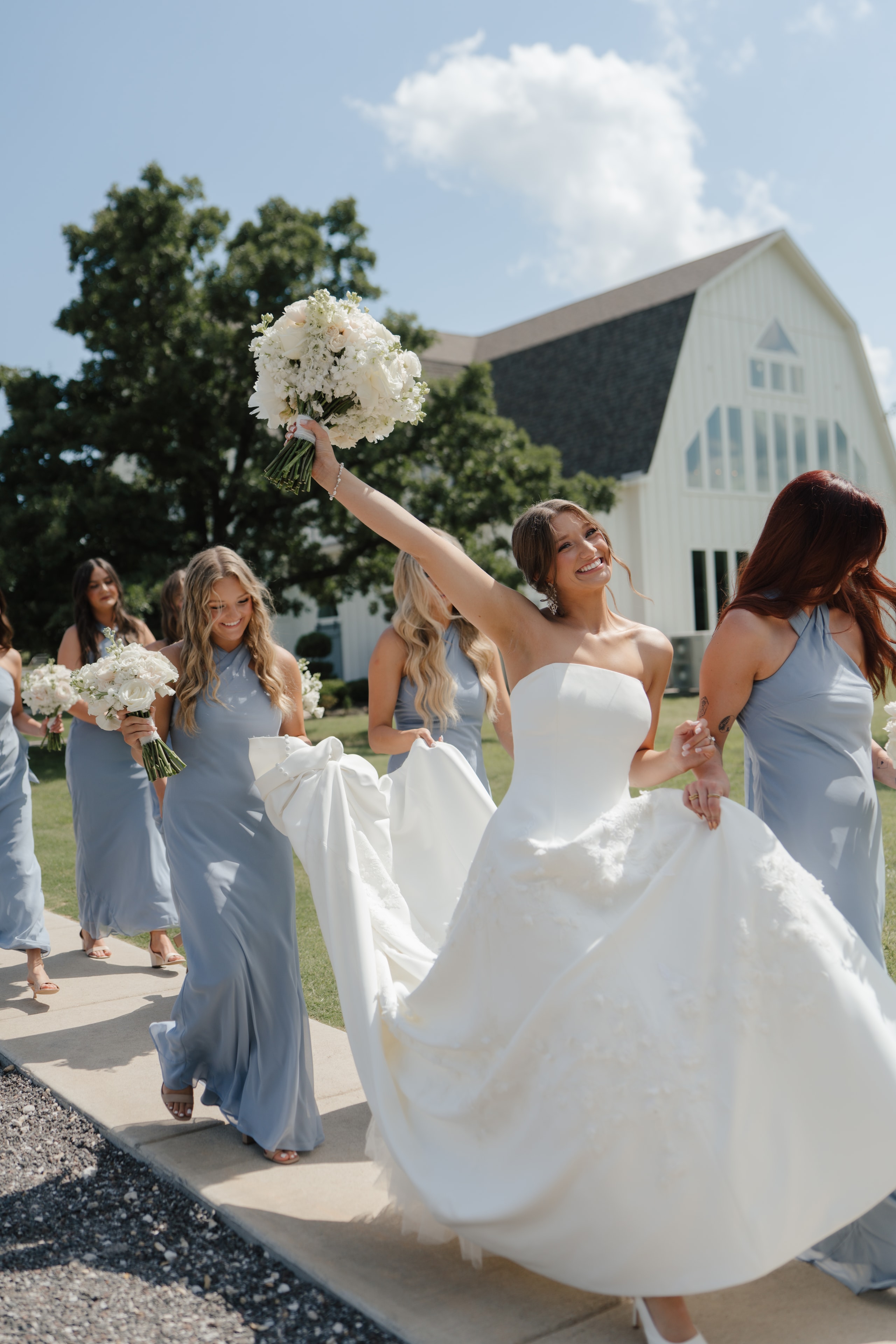 Paige celebrating with her bridesmaids in dusty blue gowns outside The French Farmhouse Venue chapel