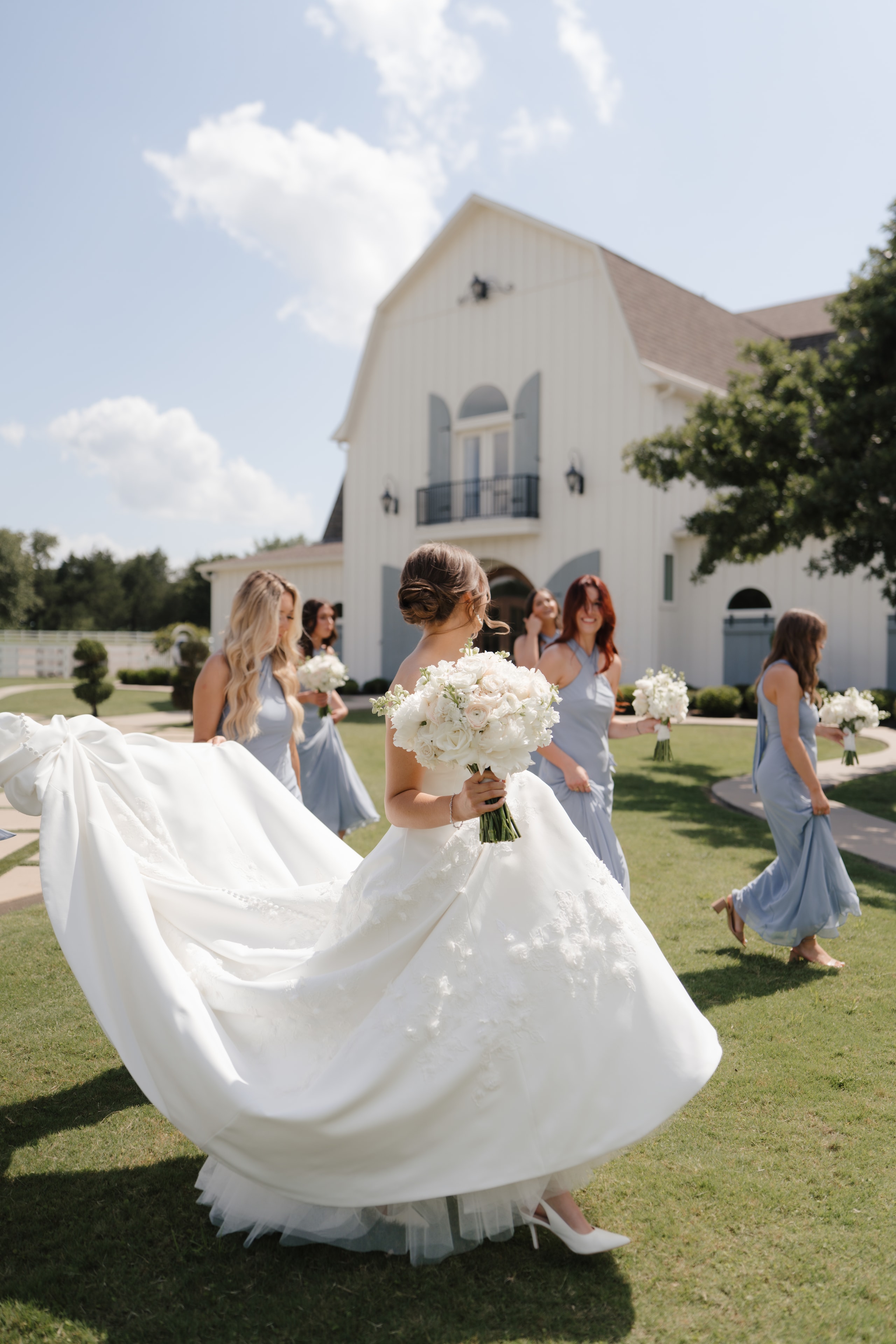 Paige and her bridesmaids in dusty blue dresses walking across the grounds of The French Farmhouse Venue
