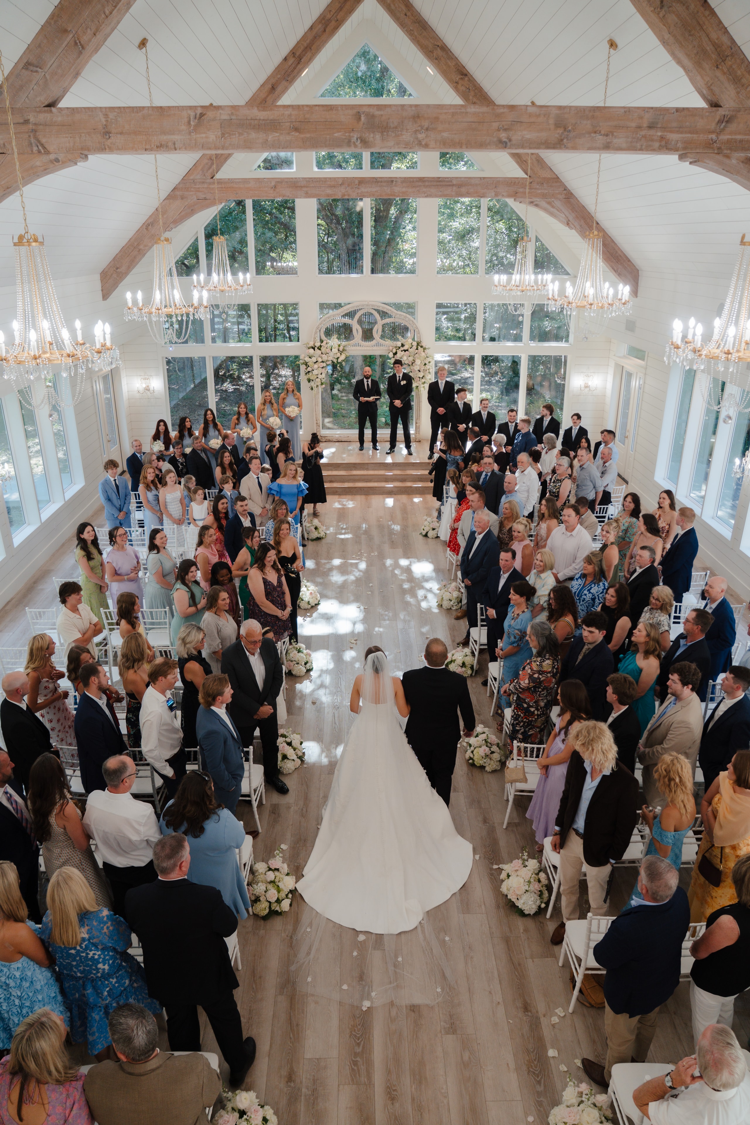 Aerial view of Paige walking down the aisle with her father inside The French Farmhouse chapel, guests standing on both sides